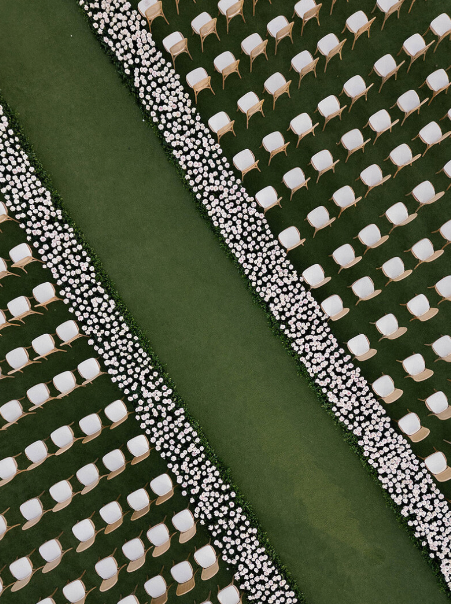 Aerial view of white chairs arranged in diagonal rows on a green lawn for an outdoor ceremony.
