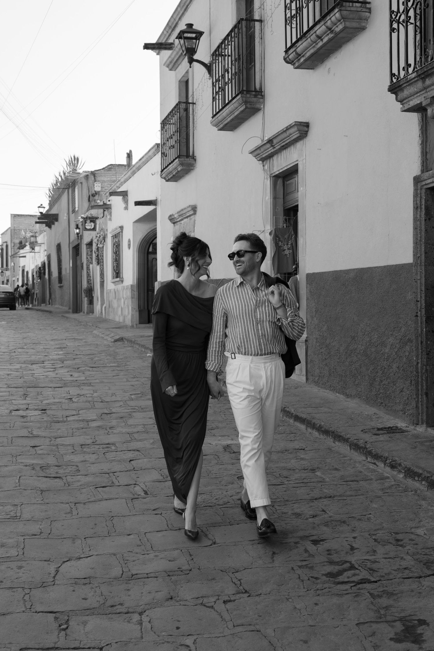 People strolling down a historic cobblestone street with white buildings and iron balconies.