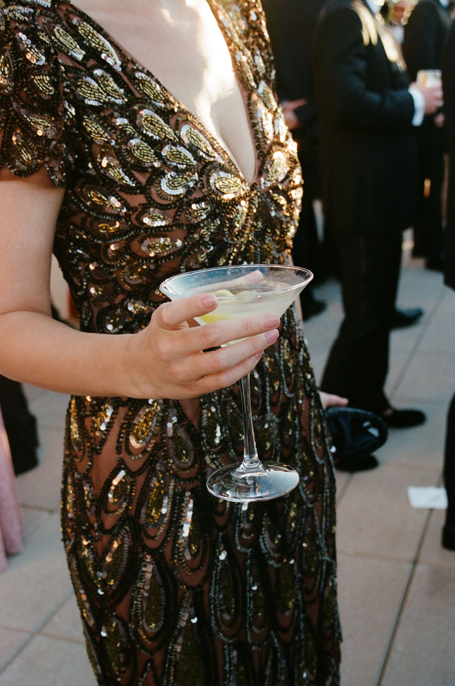 Person in a sequined black and gold dress holding a champagne glass at an event.