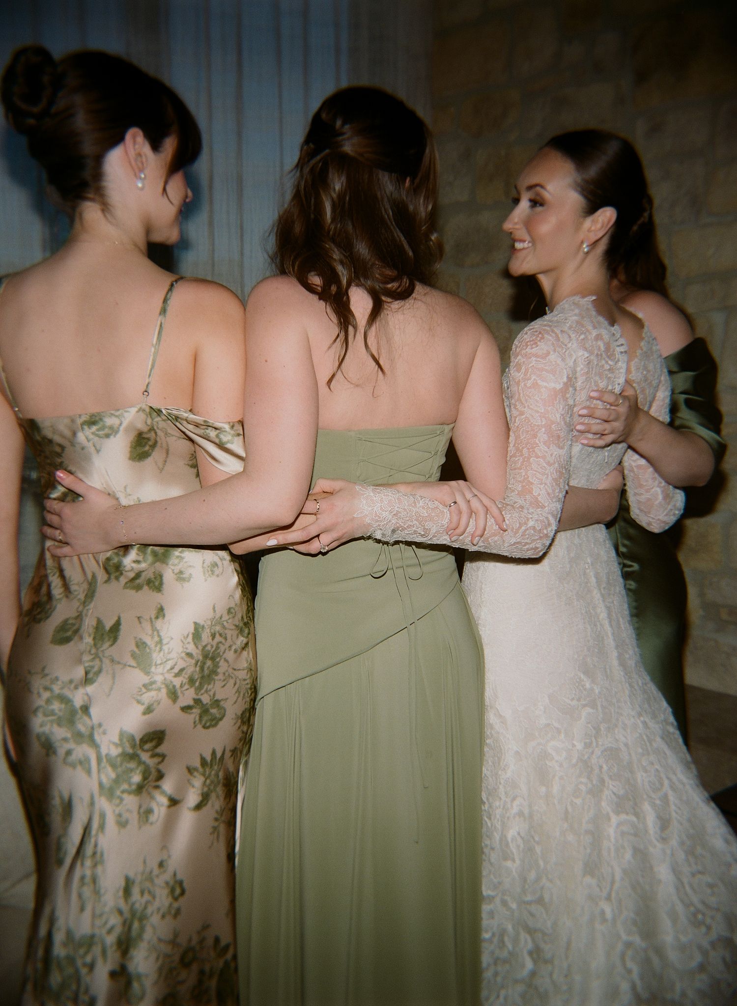 Bridesmaids in floral and solid dresses embrace in a candid moment.