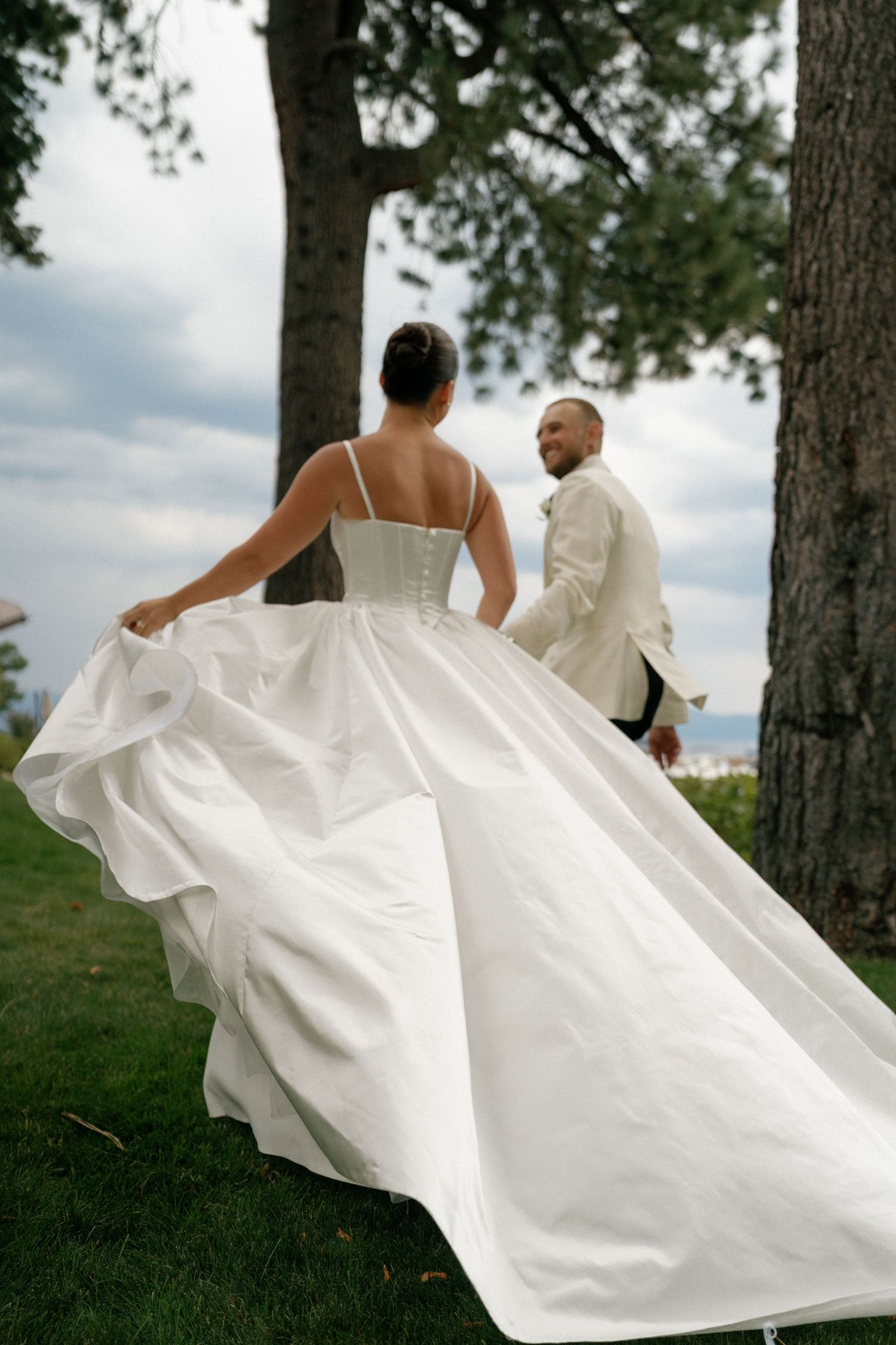 Wedding couple walks through pine trees as bride's white dress flows dramatically behind them.