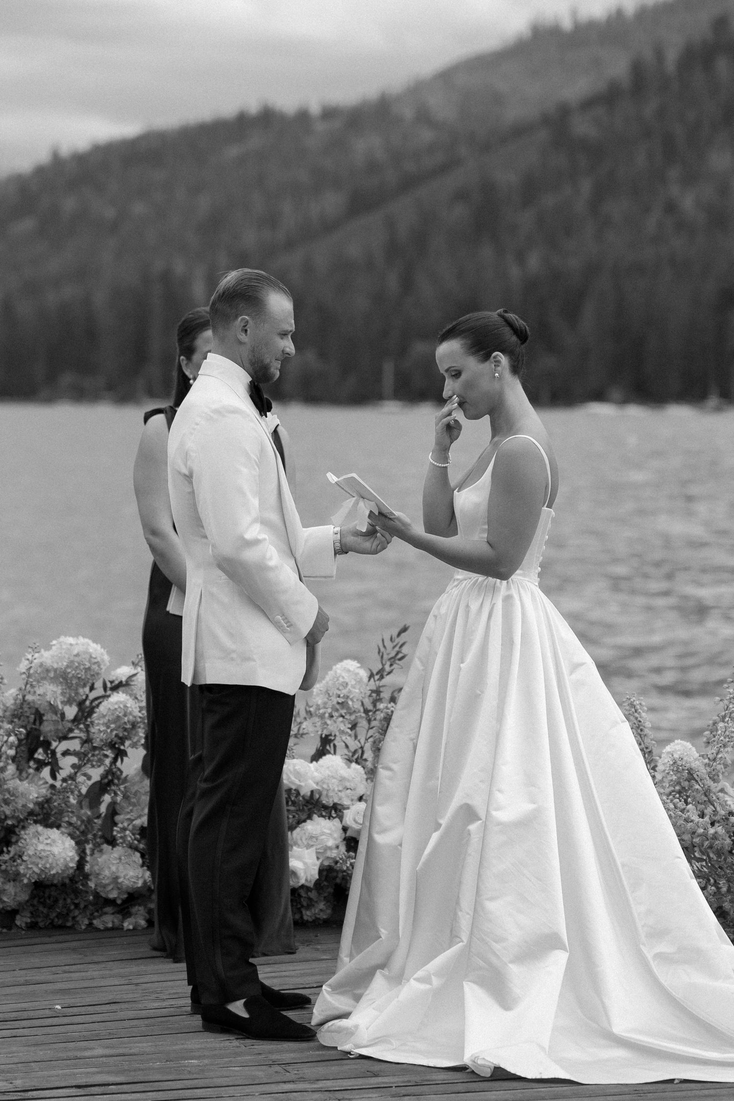 Wedding couple sharing intimate moment on dock with mountain lake backdrop.