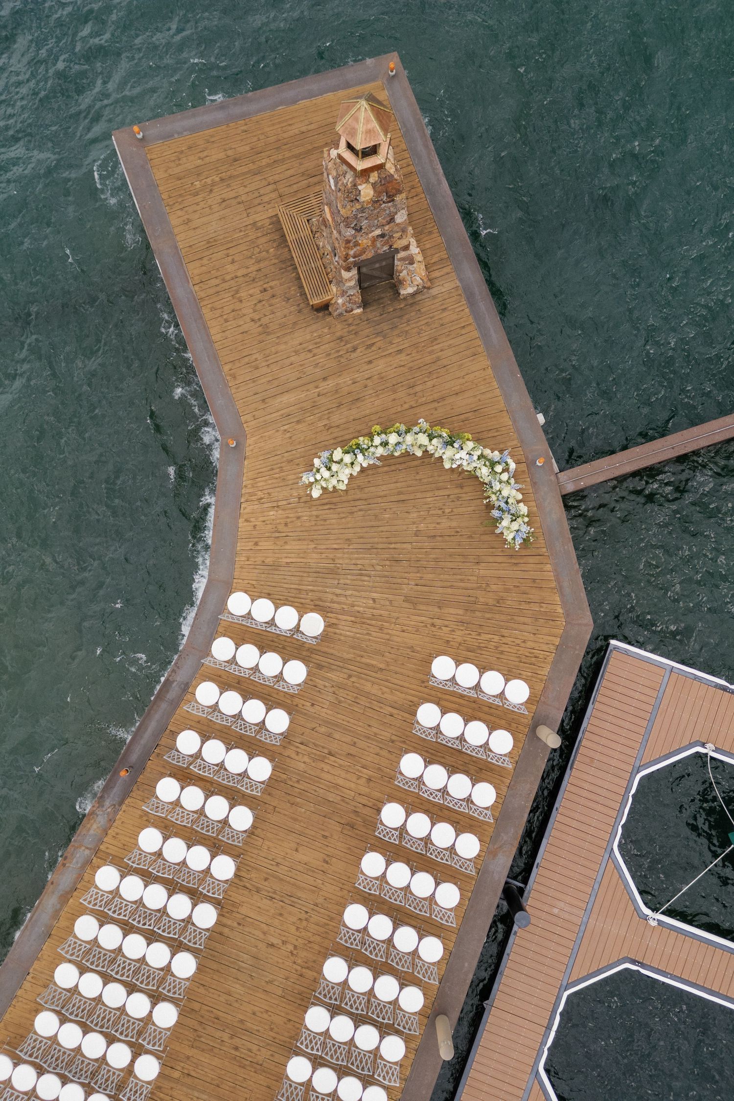 Wooden dock seating arrangement with white chairs set up in rows over water.