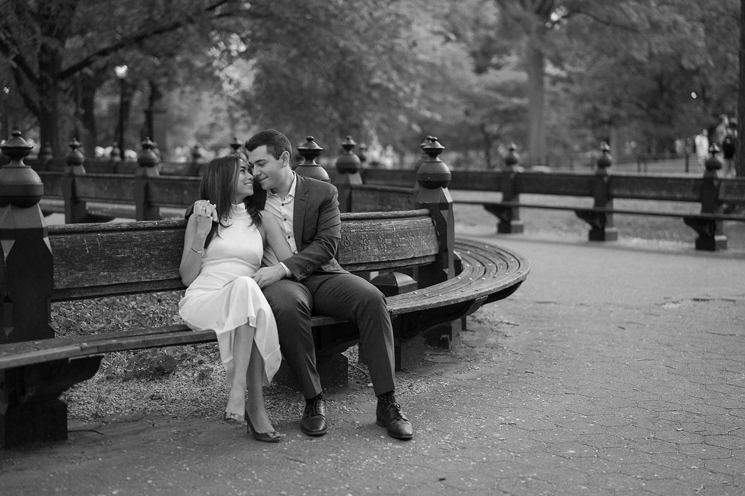 A romantic black and white scene in a park with a couple sitting together on a curved bench.