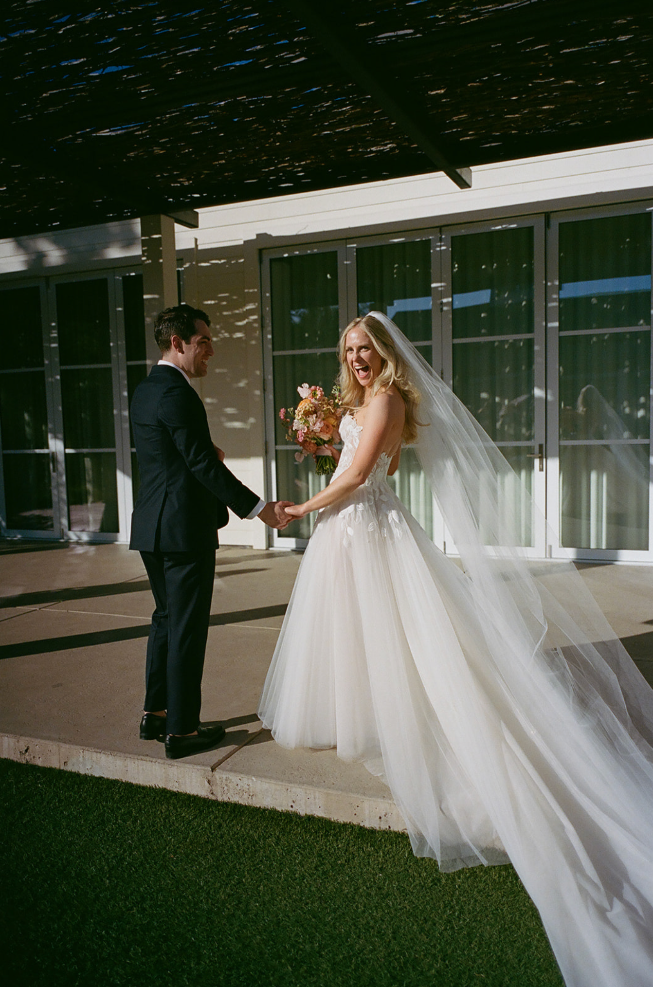 Outdoor wedding moment captured with flowing veil and modern building backdrop.