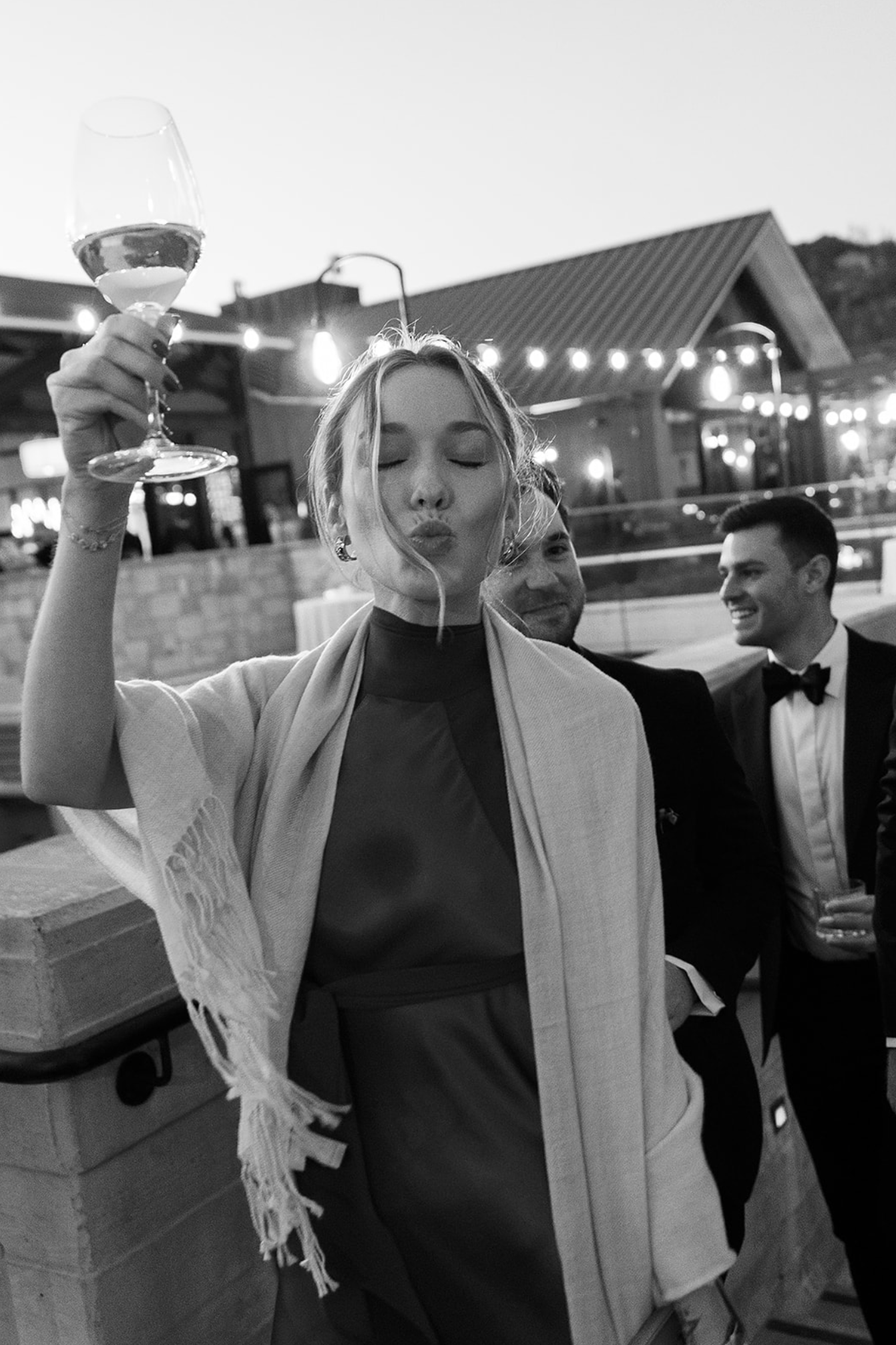 Evening celebration with champagne toasts under string lights at outdoor venue.