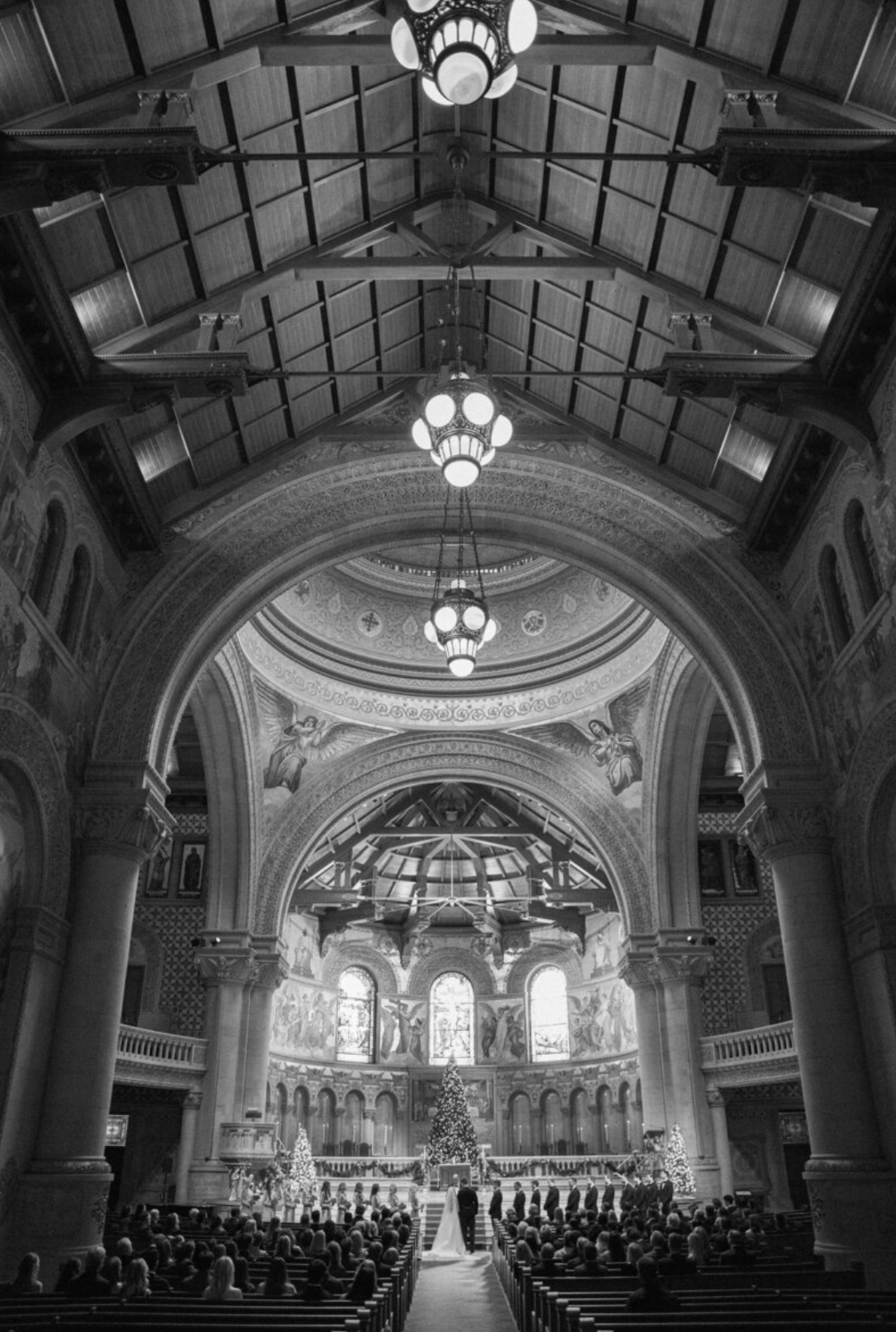 Interior of a historic church with vaulted ceilings and chandeliers during a wedding ceremony.