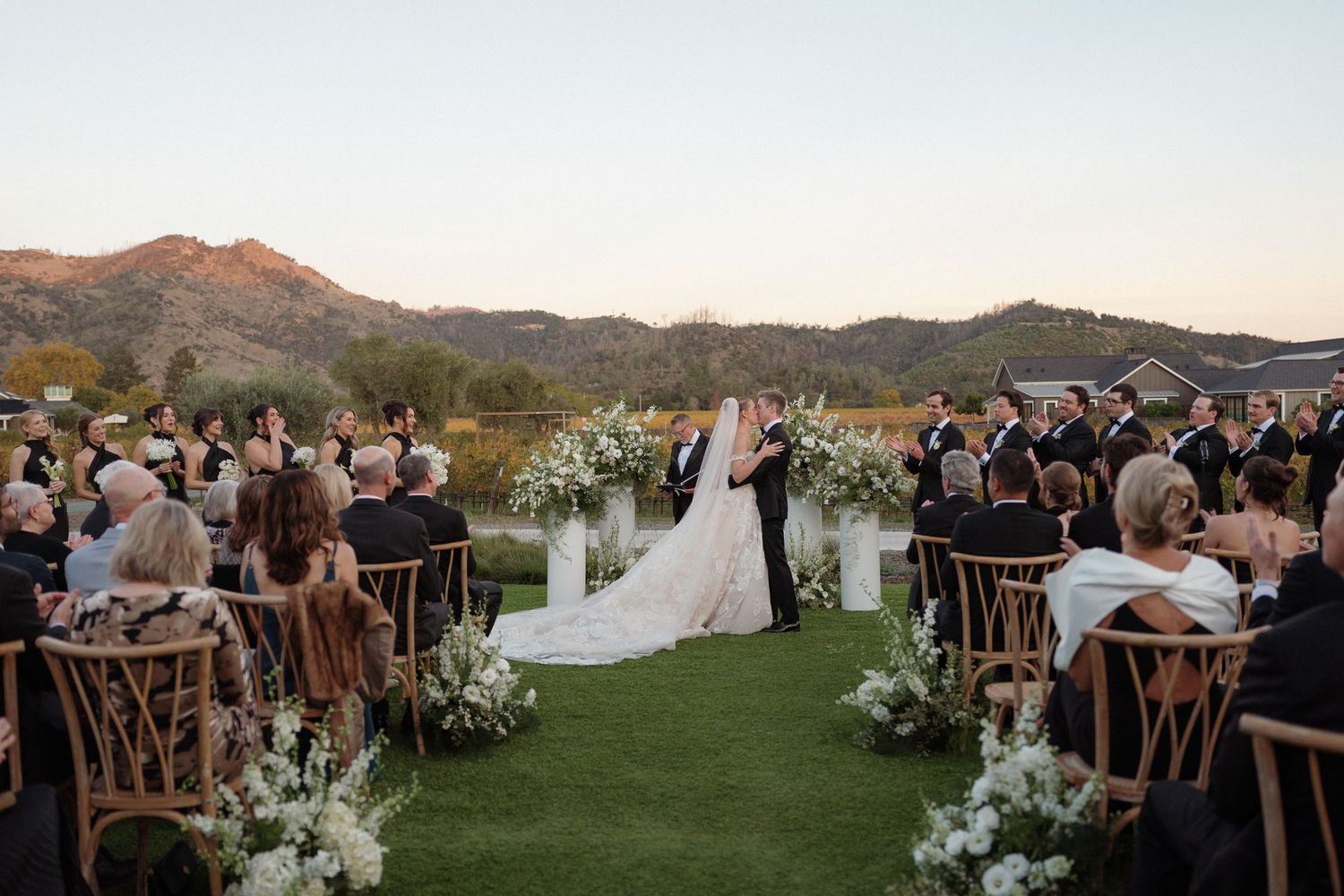 Panoramic view of an outdoor wedding ceremony setup against a mountain landscape at sunset.
