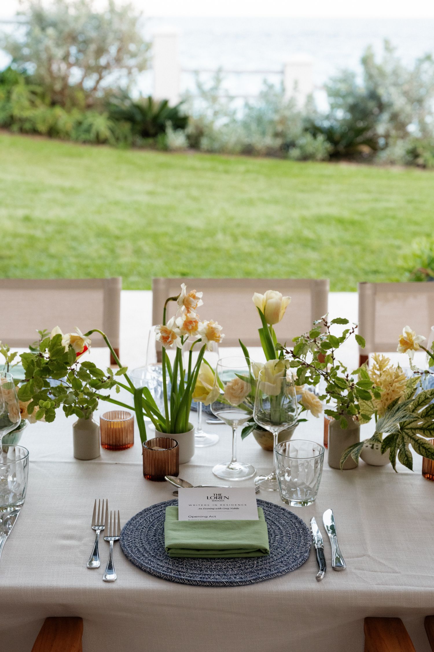 A table set for a meal outdoors with flowers and greenery in the background.