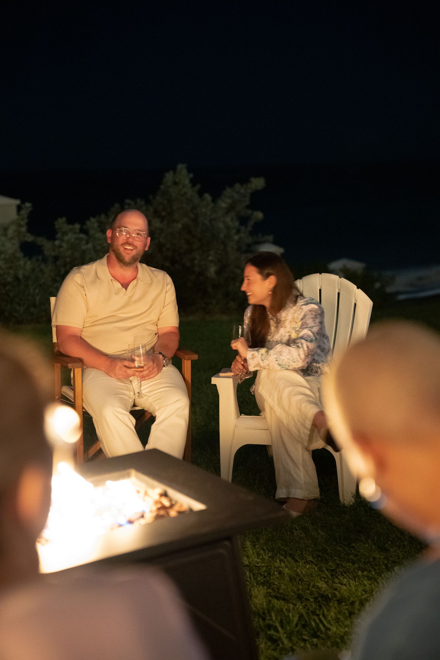A group of people sitting around a fire pit and talking at night in an outdoor setting.