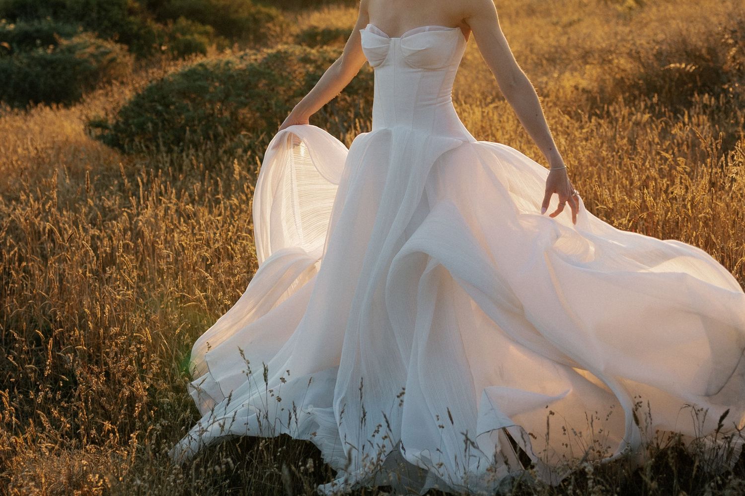 White wedding dress flowing across golden grass during sunset photoshoot.