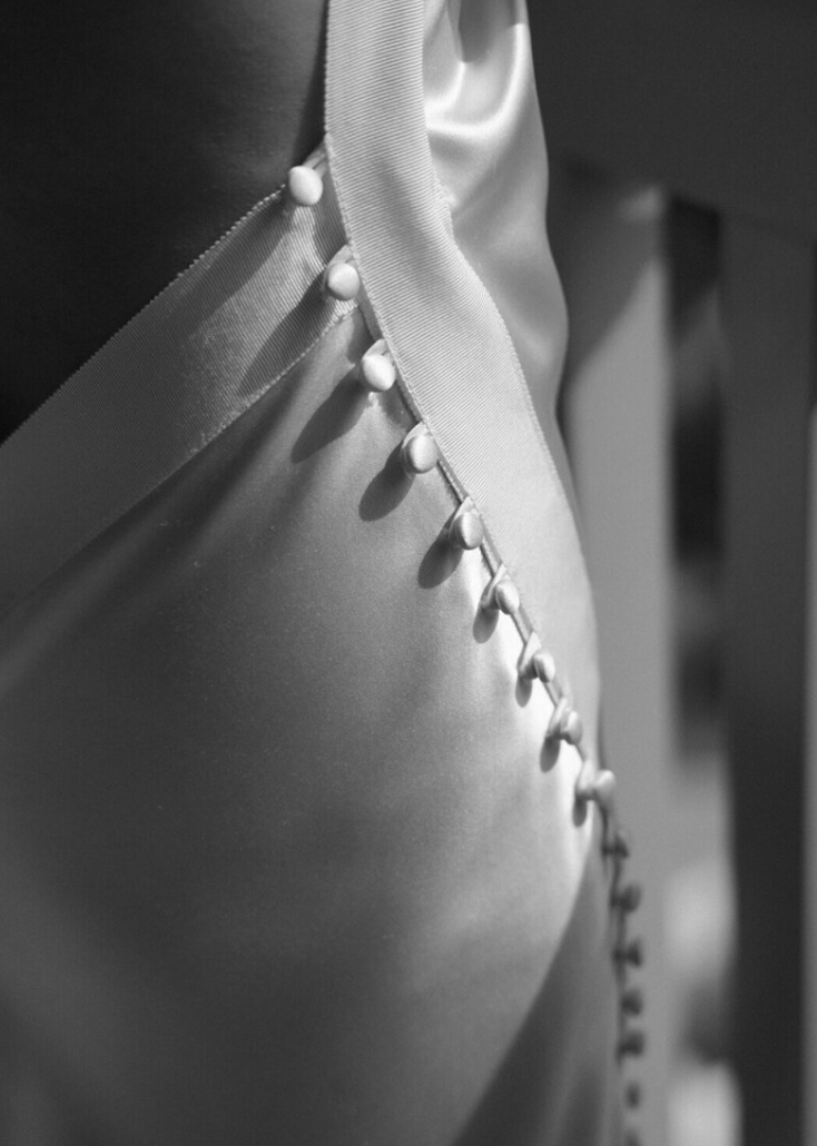 Close-up detail of buttons on the back of a white wedding dress in black and white.