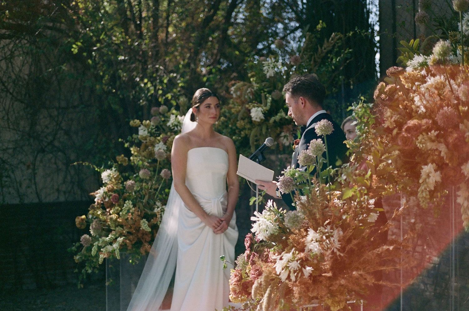 Wedding ceremony moment surrounded by peach-colored floral arrangements in garden setting.