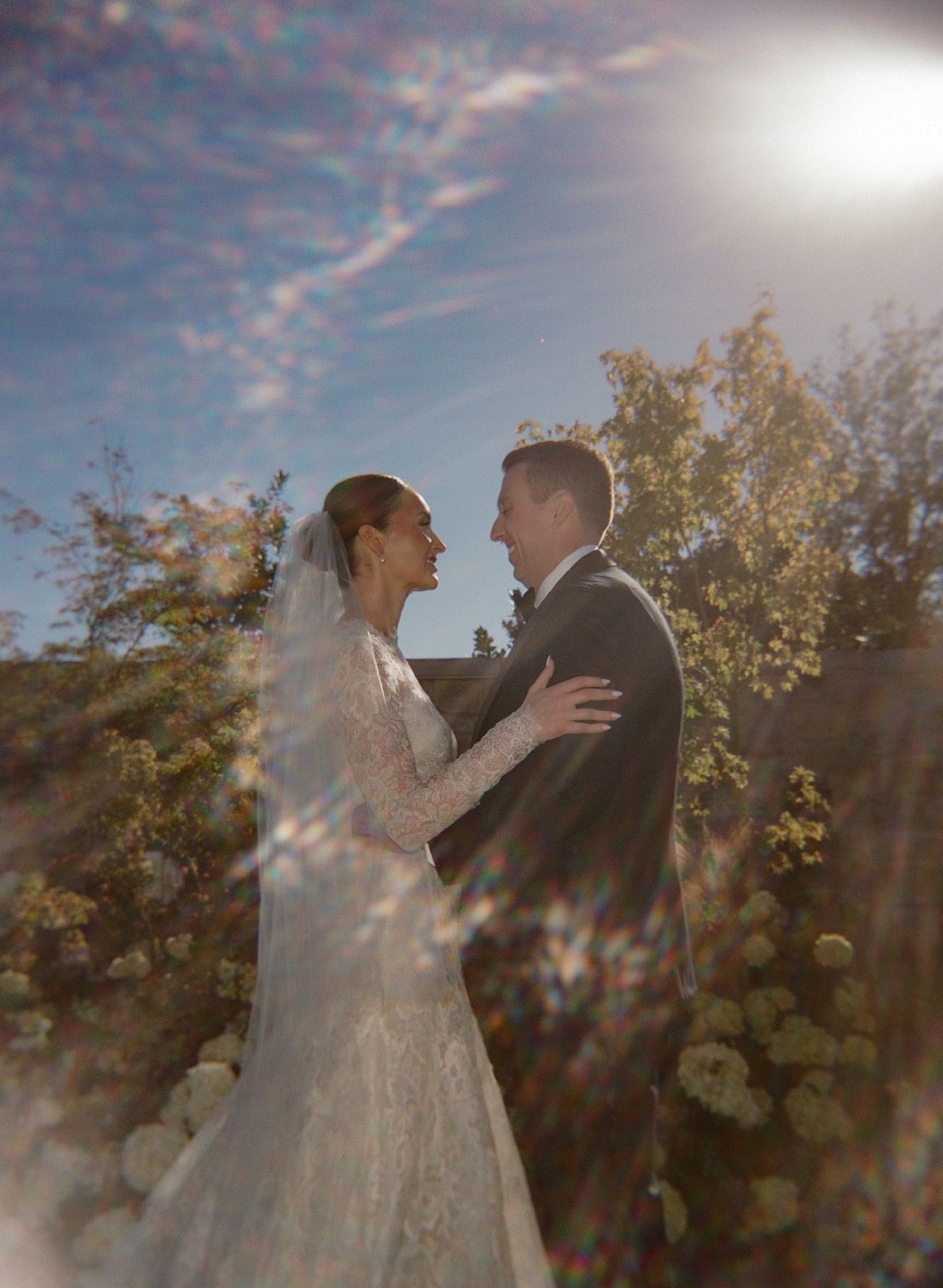 A romantic wedding portrait backlit by golden sunlight among autumn trees.