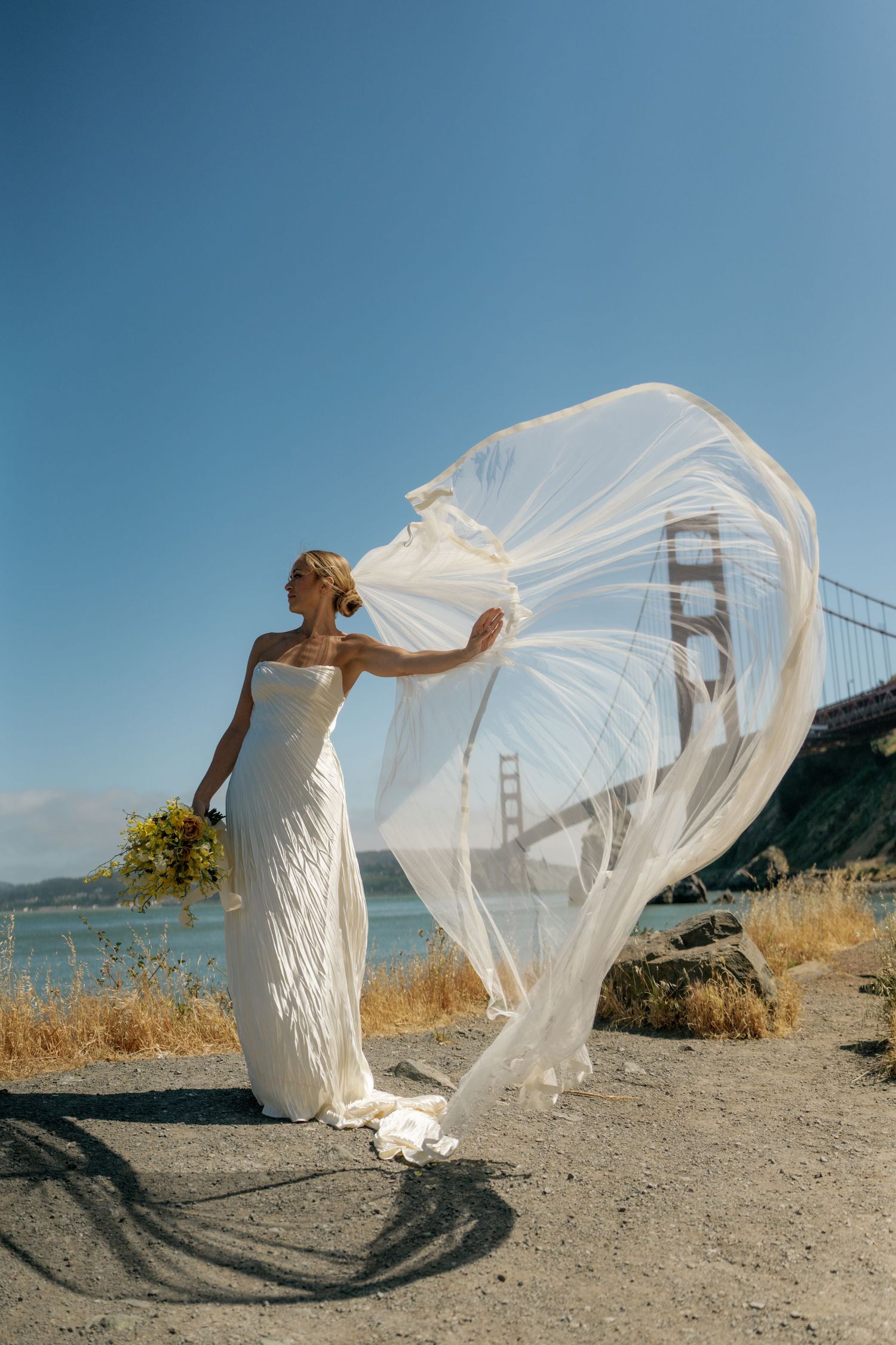 Bride's veil flowing dramatically in wind with Golden Gate Bridge in background.