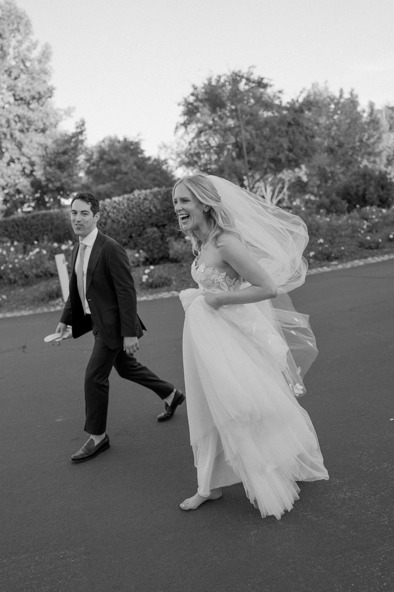 Black and white photo of a joyful moment with a bride's veil flowing in the wind.