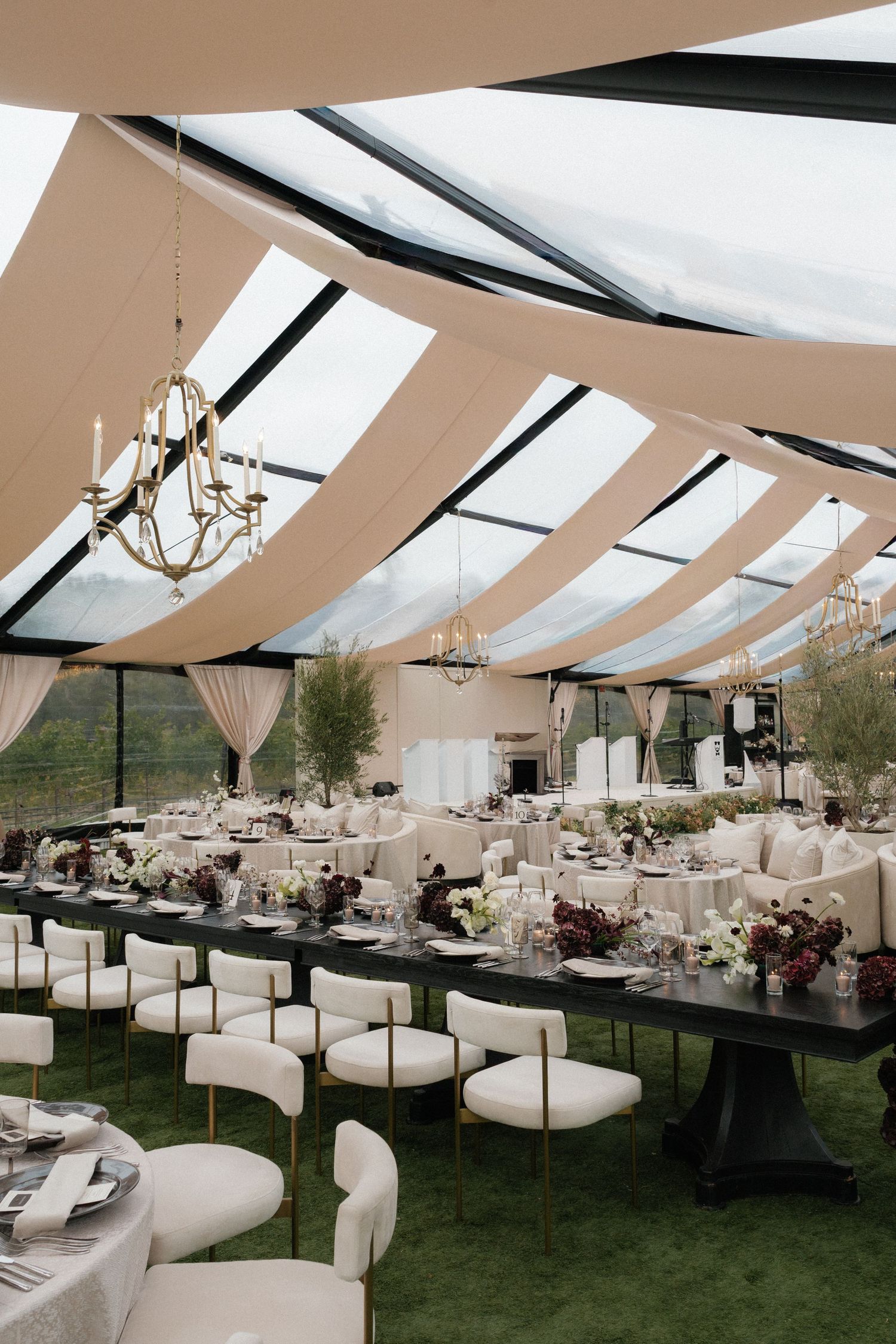 Wedding reception tent with white draping, elegant table settings and lounge furniture.