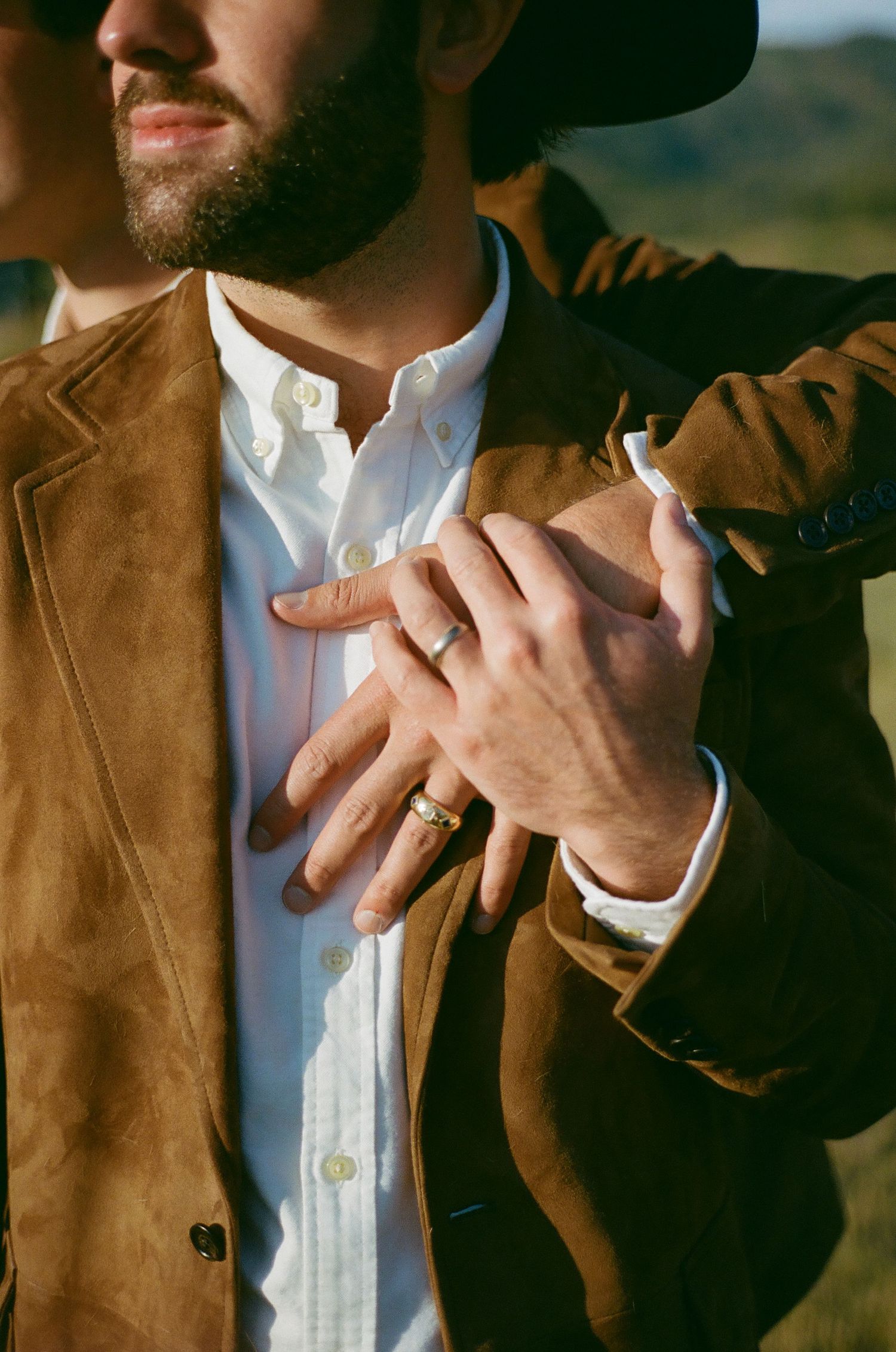Close-up detail shot of hands wearing western-style attire with suede jacket.