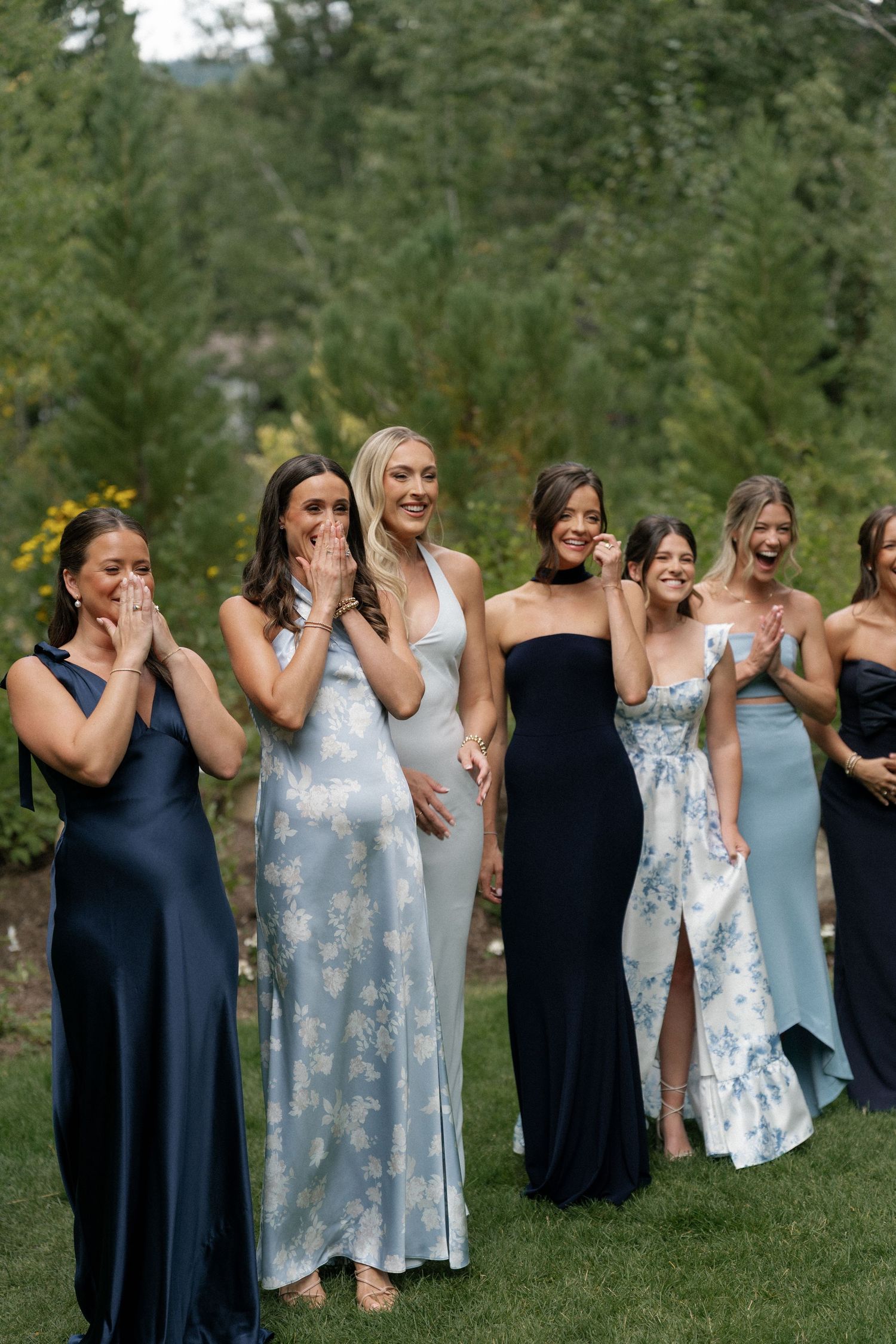 Bridesmaids in navy blue and light blue dresses pose together on a grassy hillside.