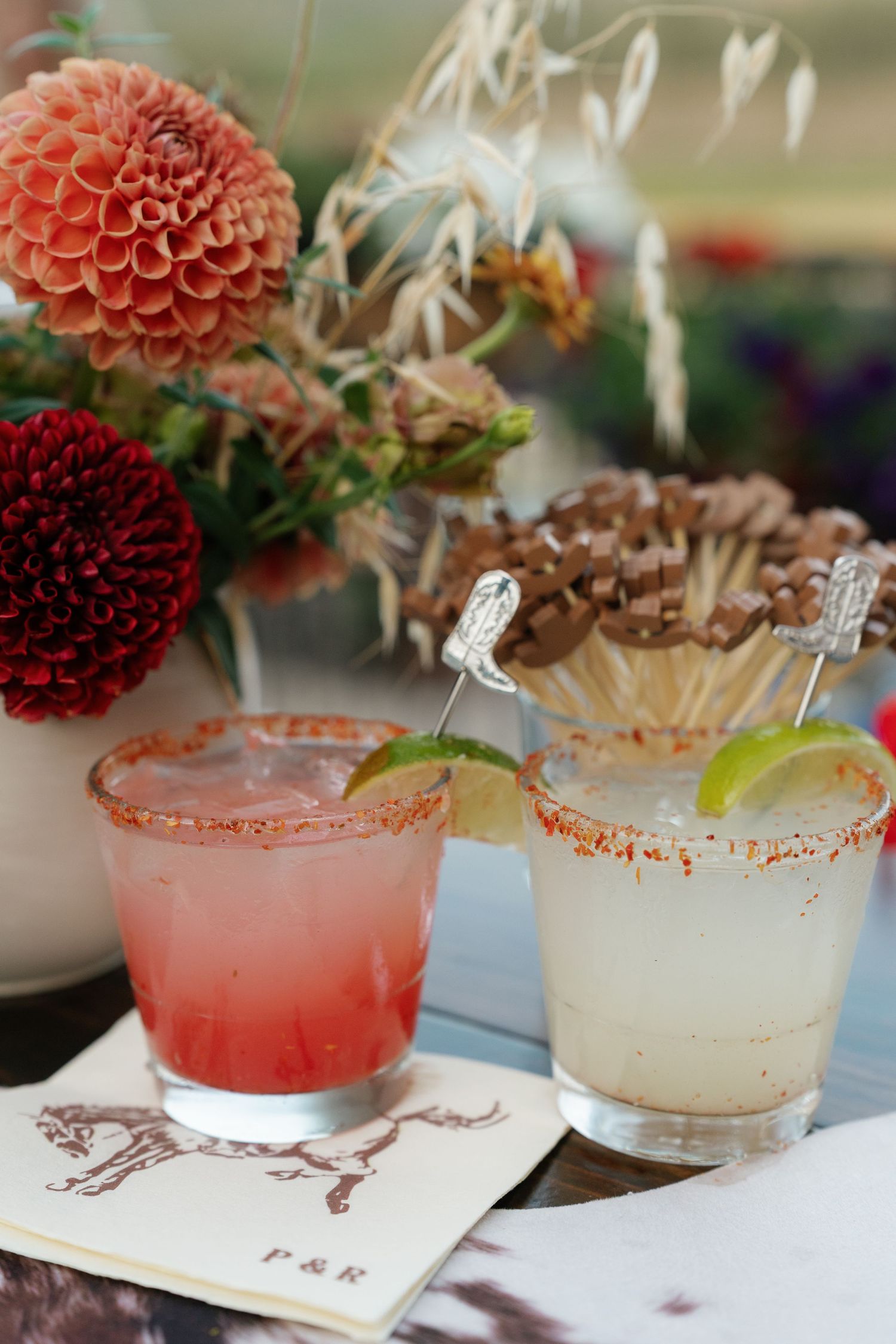 Pink and red dahlia flowers next to cocktails with sugar-rimmed glasses.
