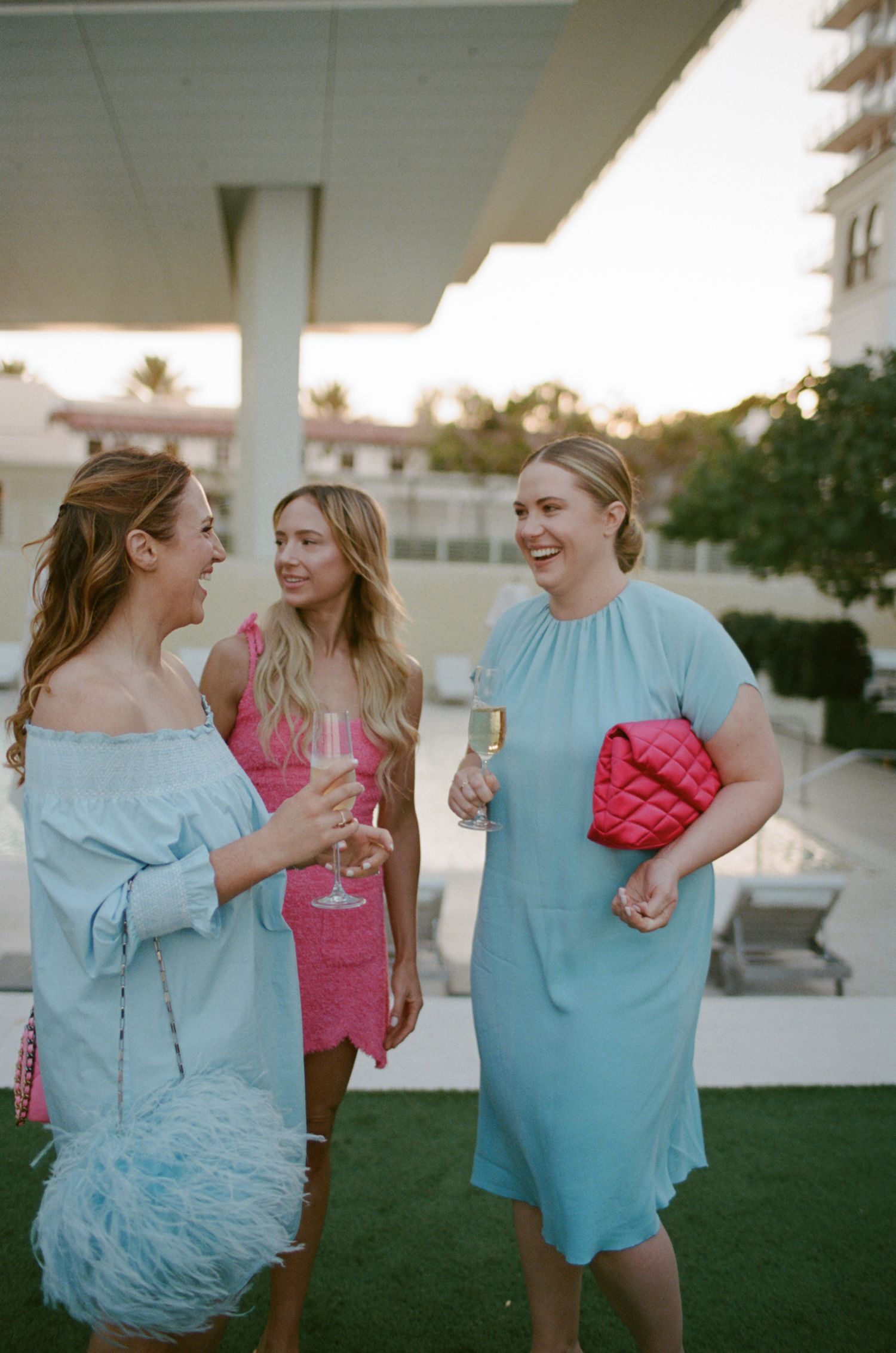 Three women in colorful dresses laughing at outdoor event.