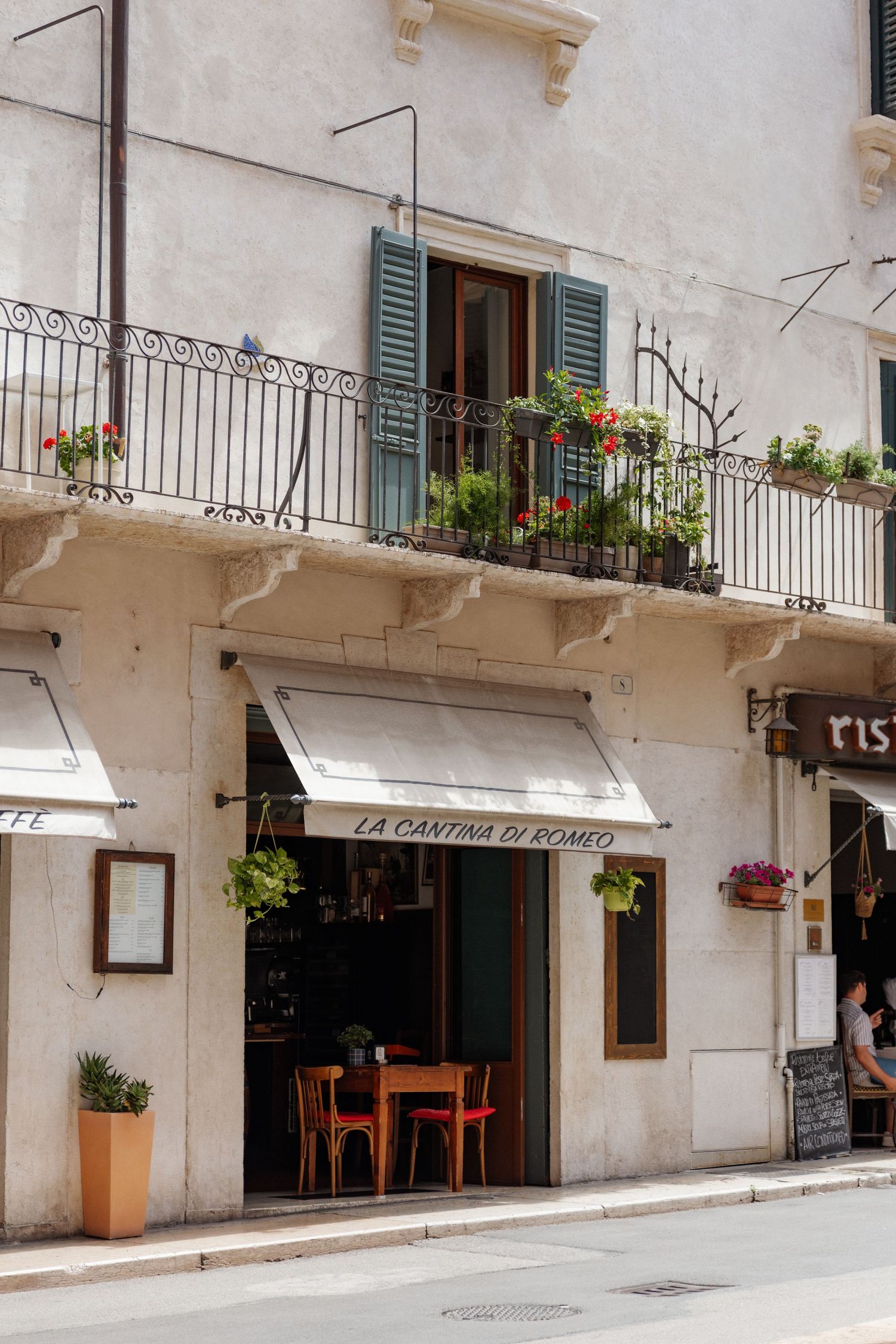 Charming Italian restaurant La Cantina Di Romeo with outdoor seating, white awning, and flower-adorned balcony on a quiet street.