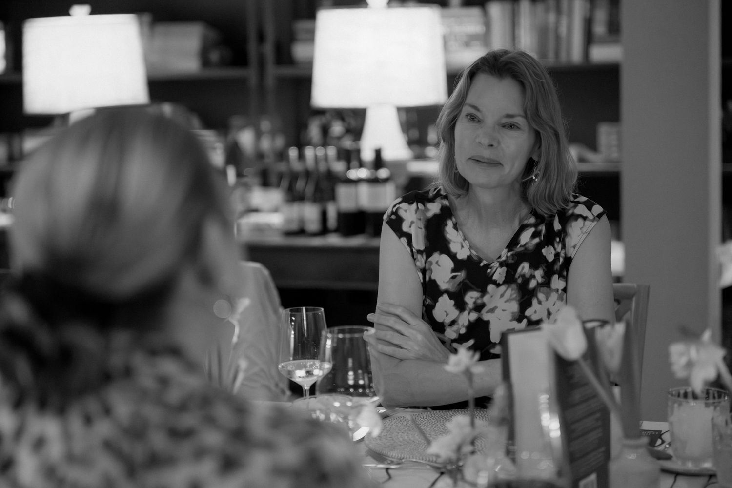 A black and white image of a woman smiling and holding a glass of wine at a bar or restaurant.