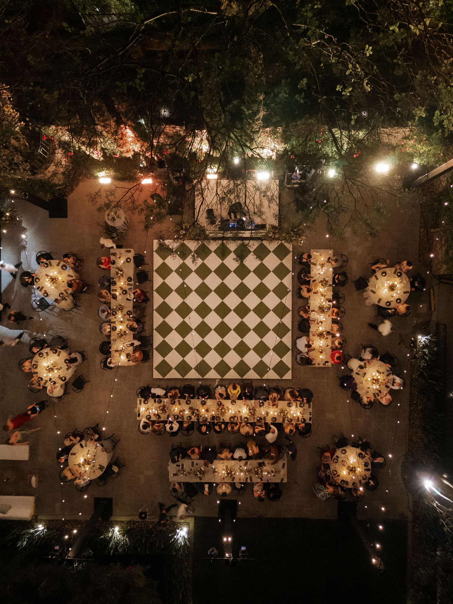 Overhead view of an outdoor wedding reception with checkered dance floor and string lights.