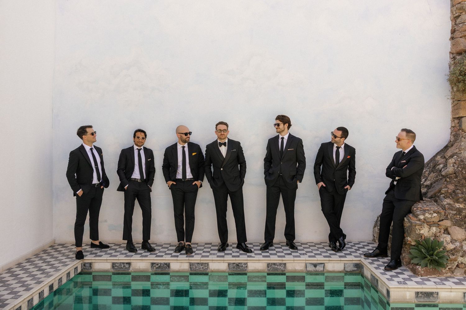 Group wearing formal attire poses against white wall with checkered floor.