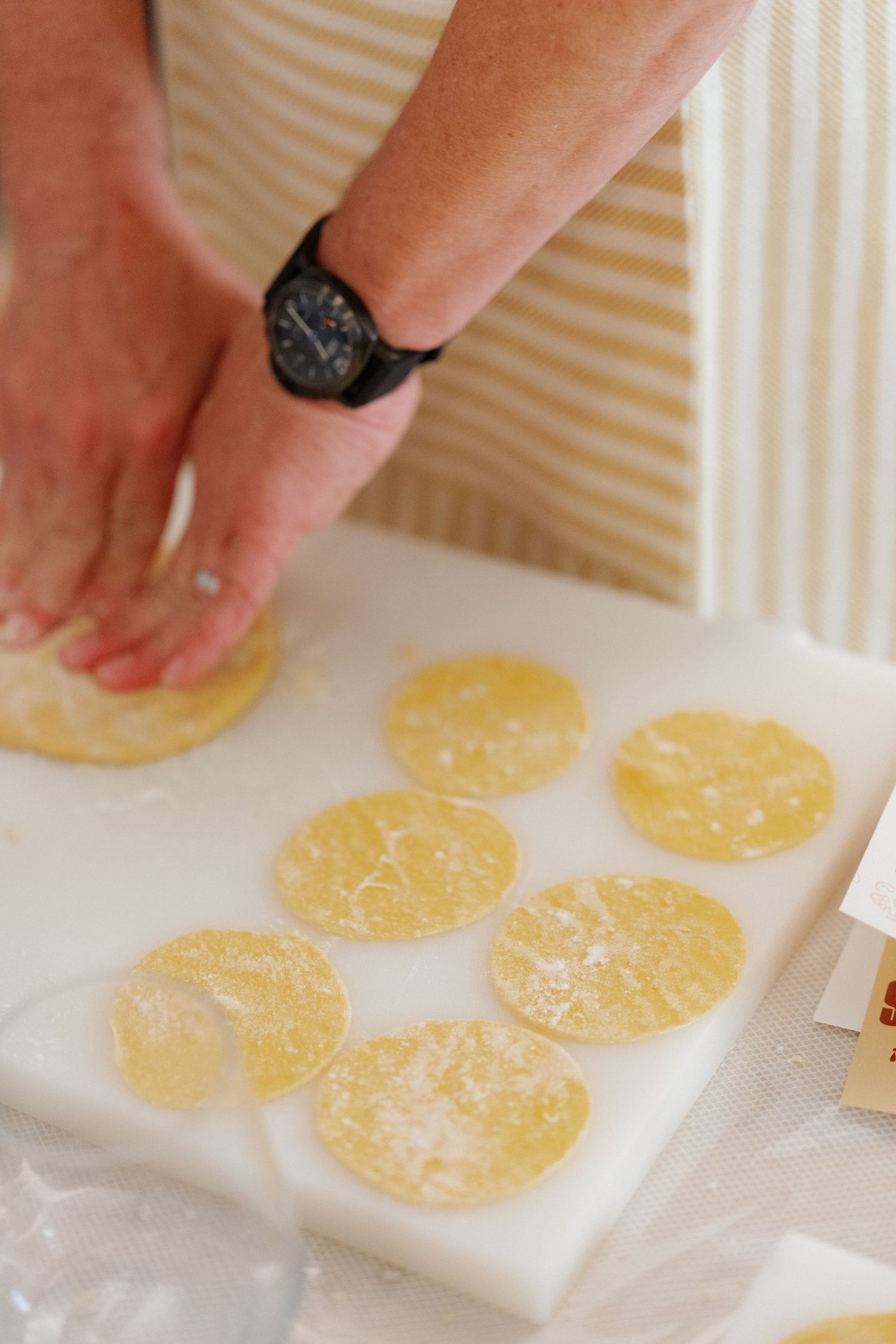 Person cutting round pasta dough circles on a white cutting board, with flour-dusted pieces ready for filling.
