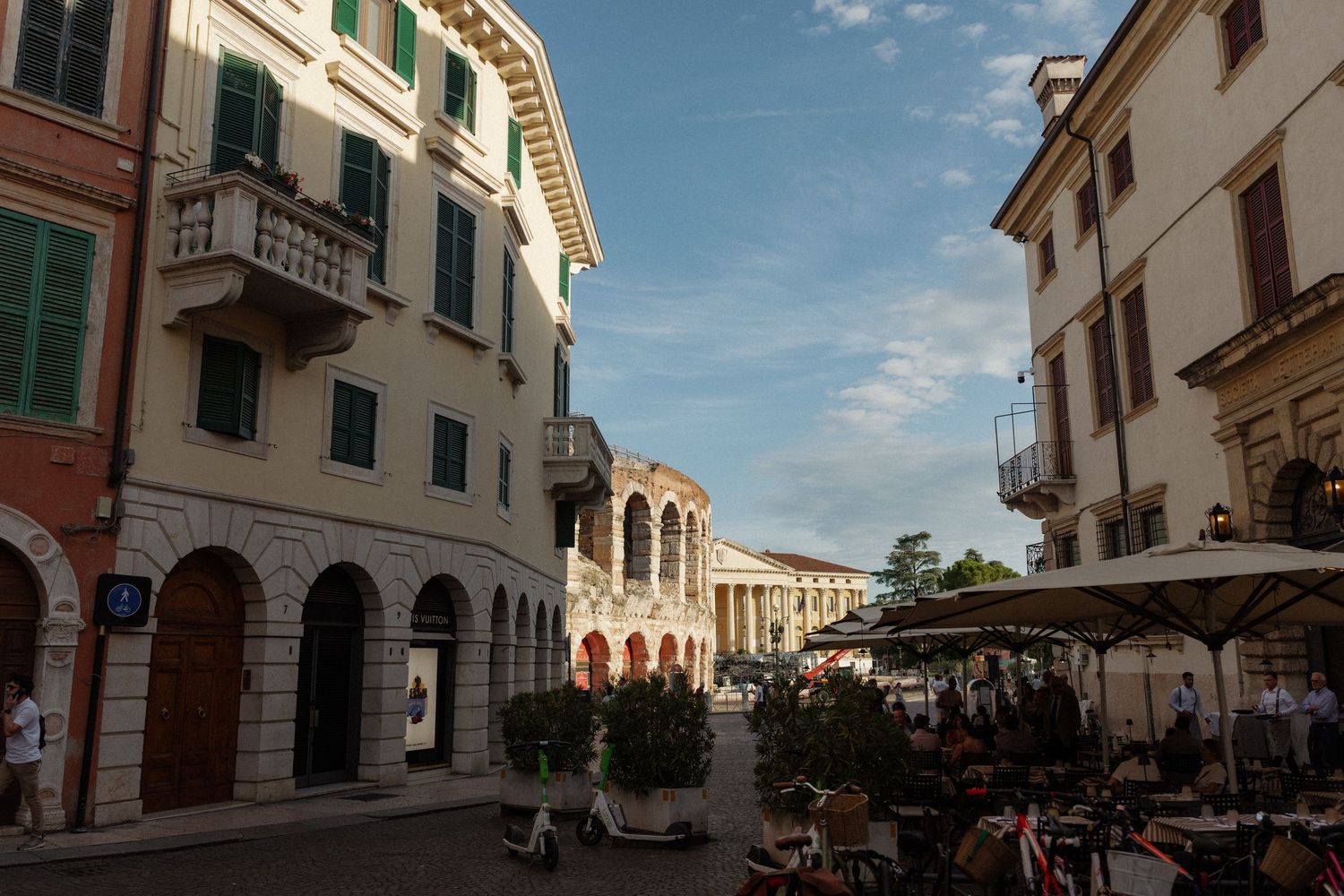 Charming Italian piazza with historic buildings, outdoor cafe seating, and Roman arena in Verona at golden hour.