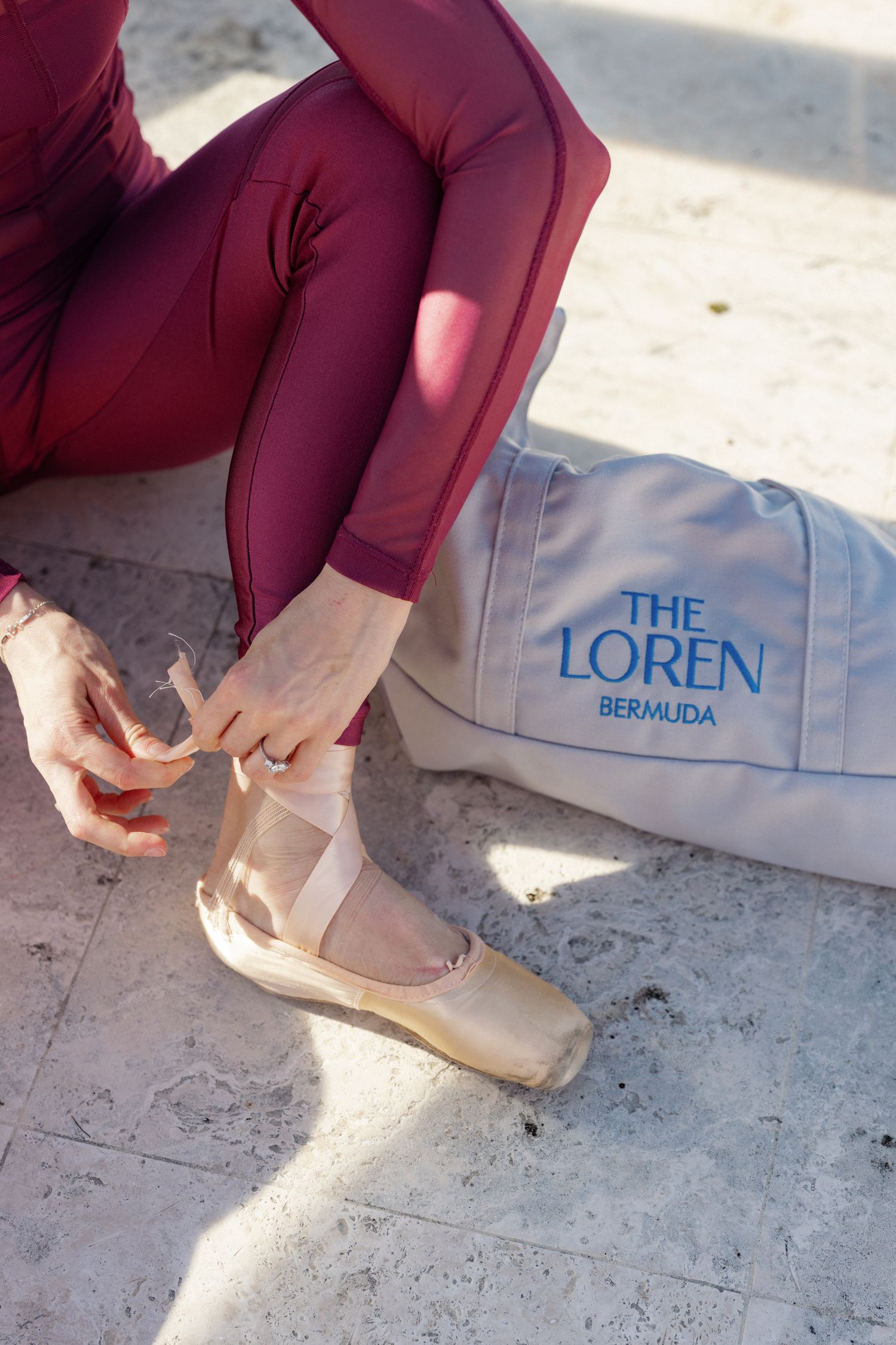 A person's legs wearing burgundy leggings and white sandals with the 'The Loren' logo.