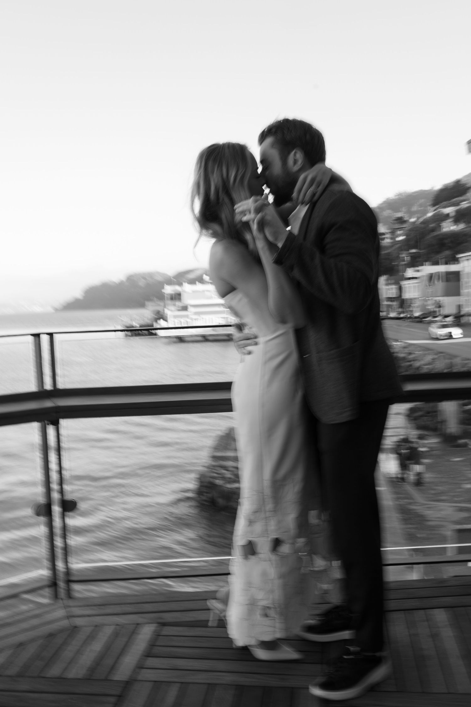 Romantic black and white moment of a couple embracing on a waterfront deck.