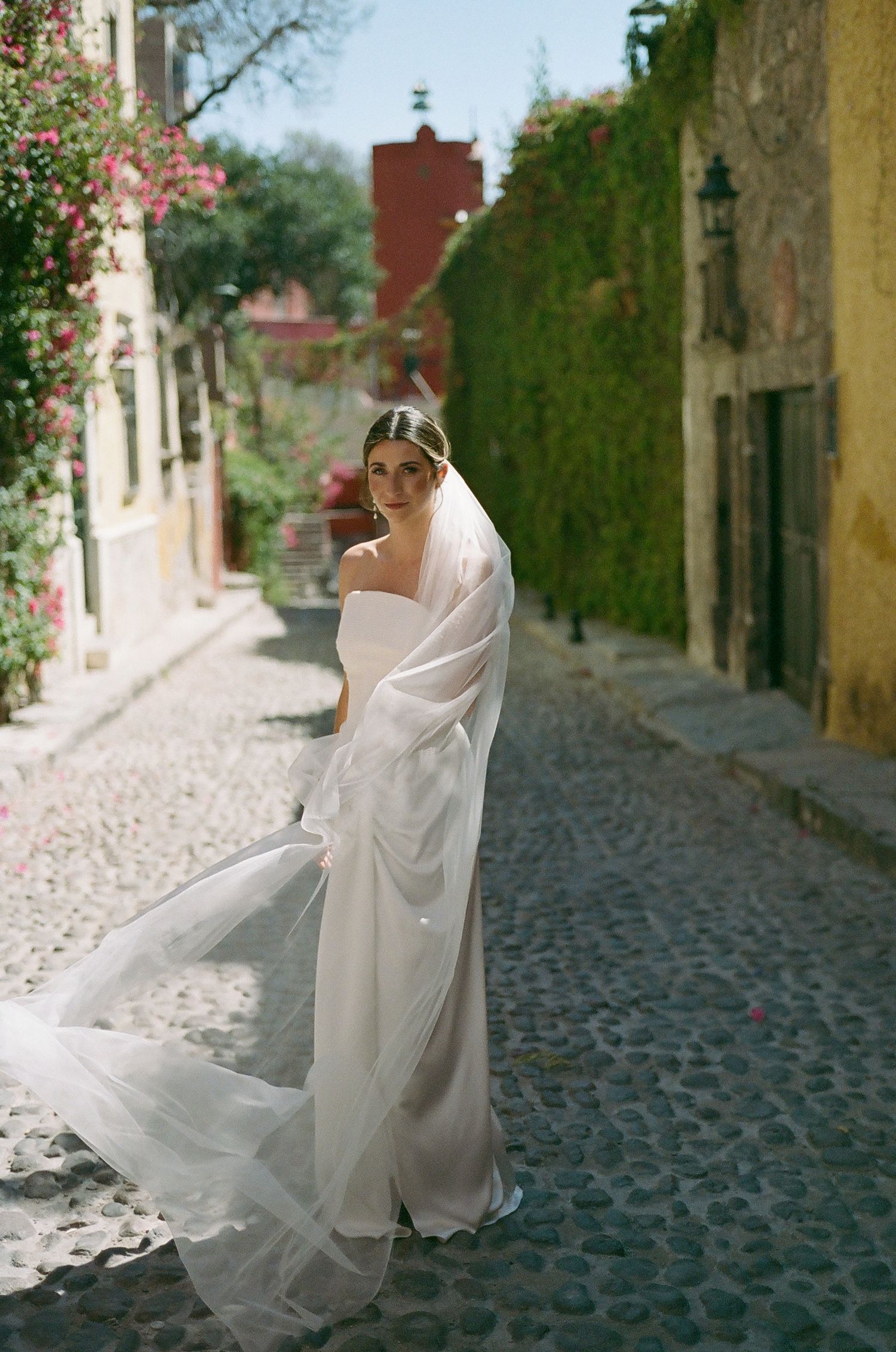 Flowing white wedding dress billowing in a charming cobblestone alley with ivy-covered walls.