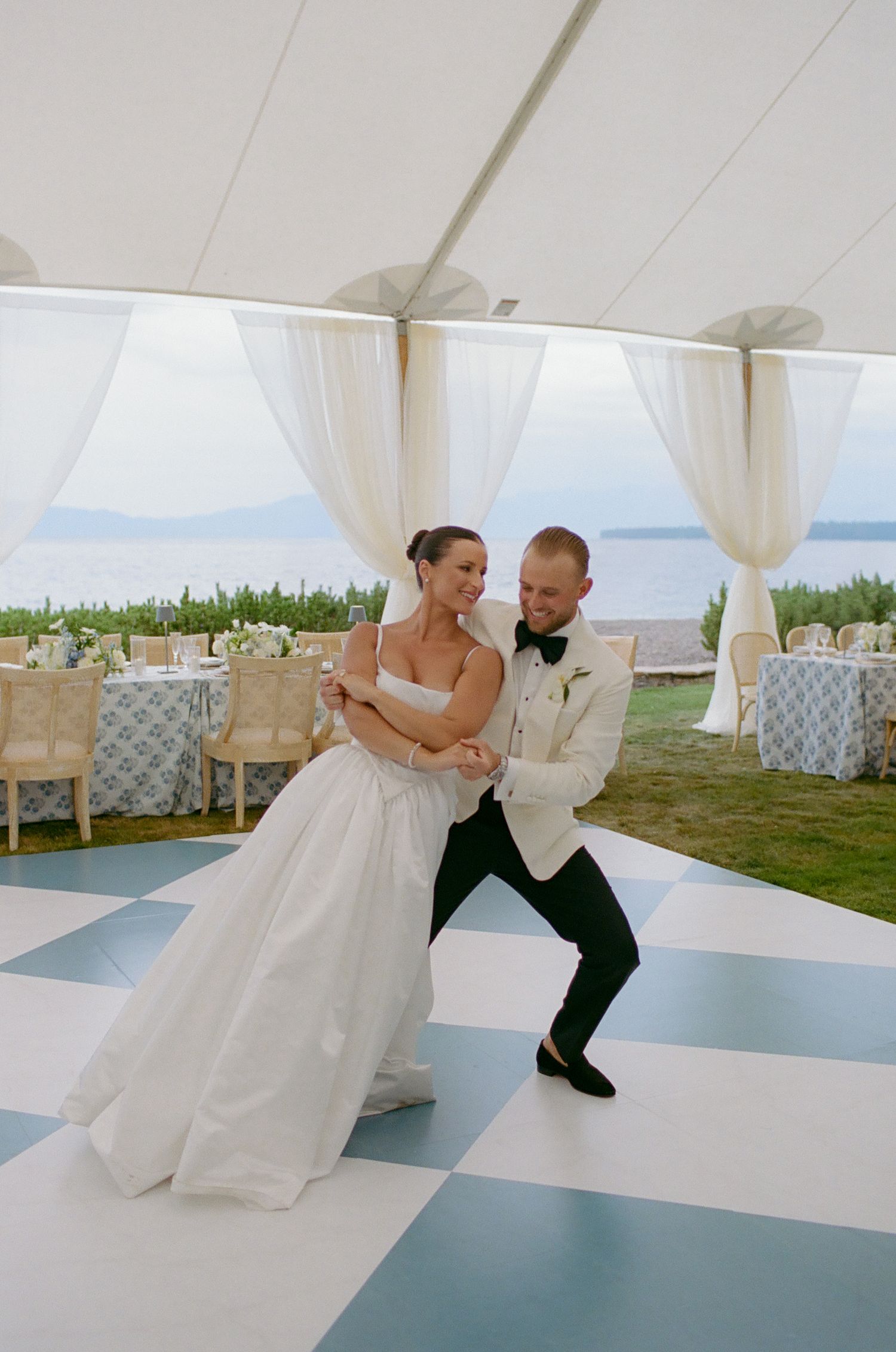Wedding couple performing a choreographed dance move on a striped dance floor under white tent.