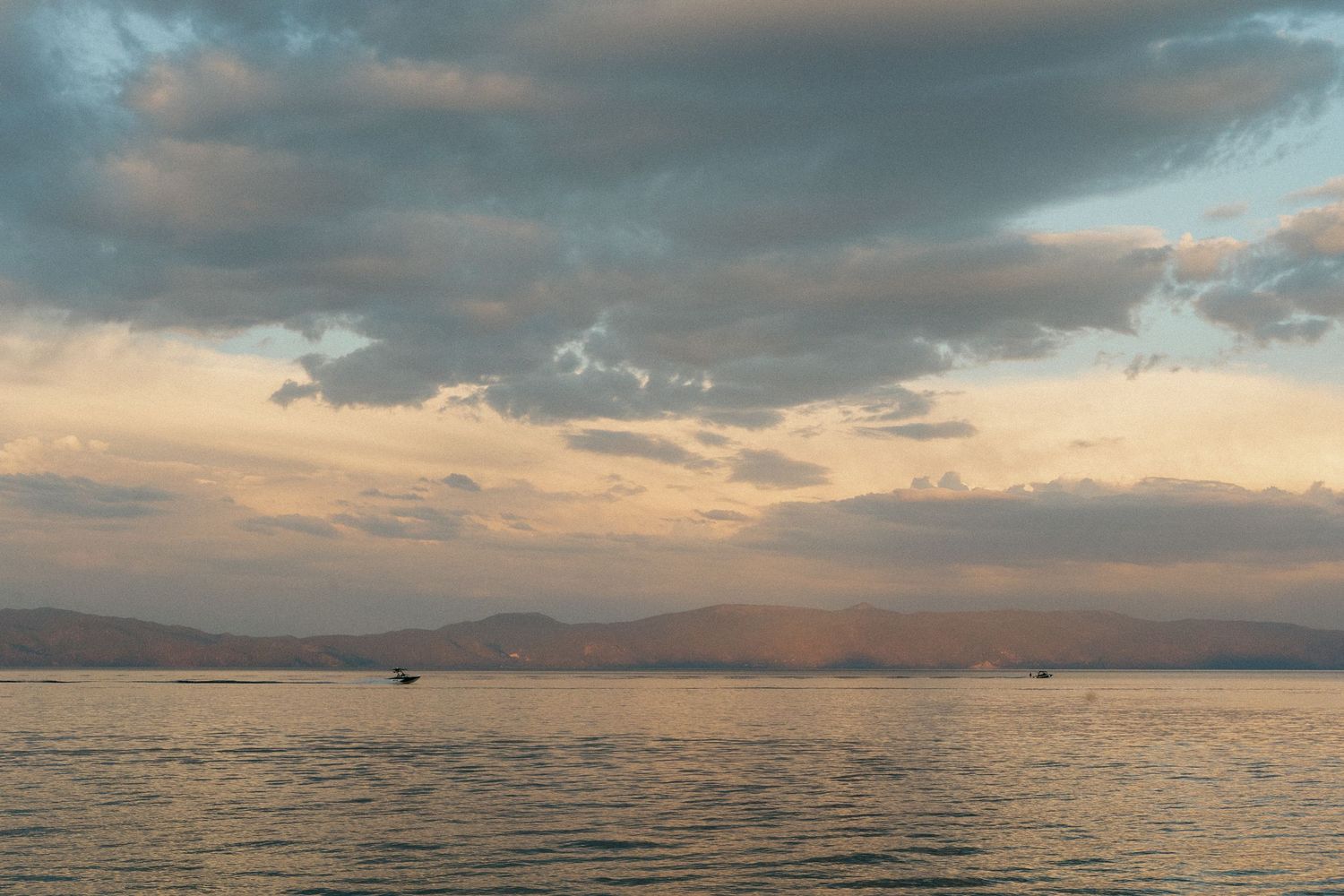 Dramatic sunset sky over calm waters with mountains silhouetted in the distance.