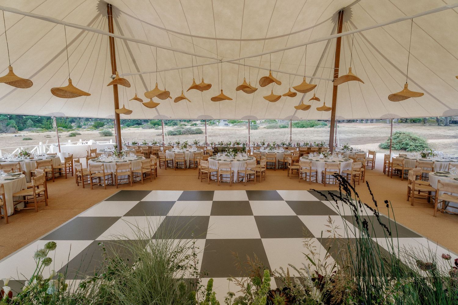 Interior of elegant wedding reception tent with checkered dance floor and table settings.