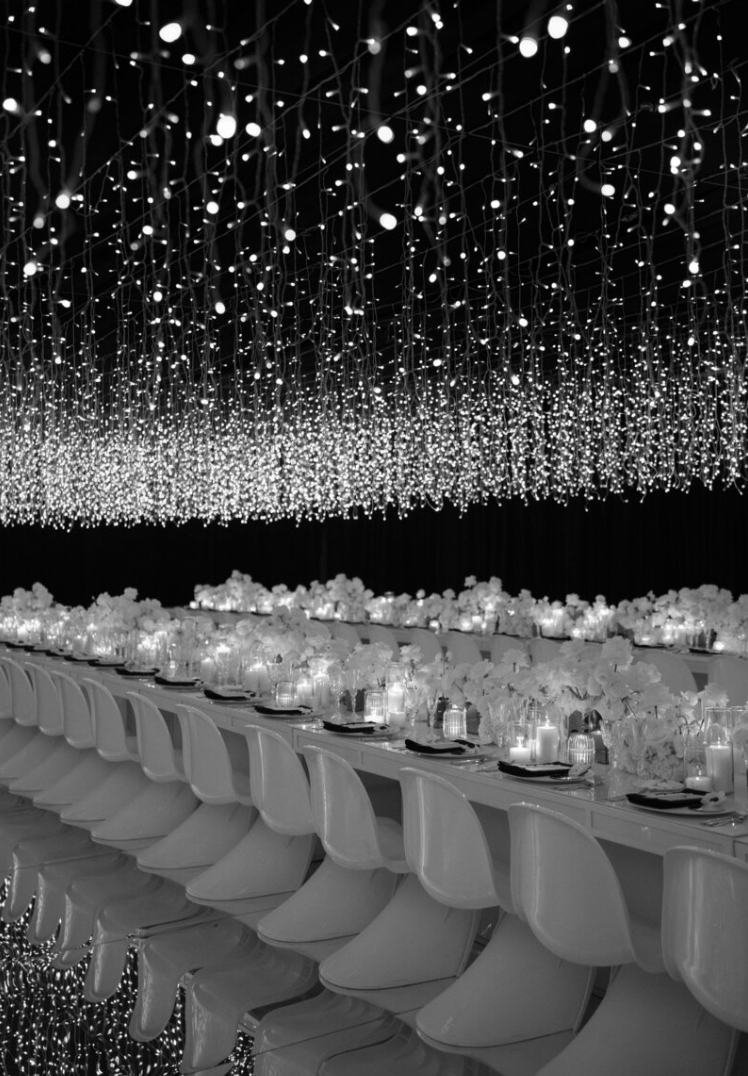An elegant reception setup with white chairs and hanging lights creating a magical starlit atmosphere.