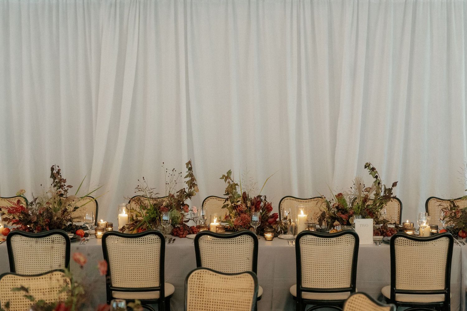 Elegant reception tables decorated with floral centerpieces against a light gray backdrop.