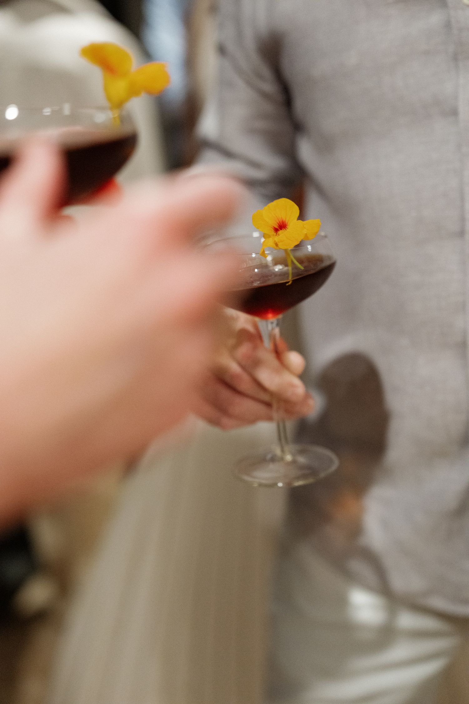 A hand holding a glass of red wine with yellow flowers floating on the surface.