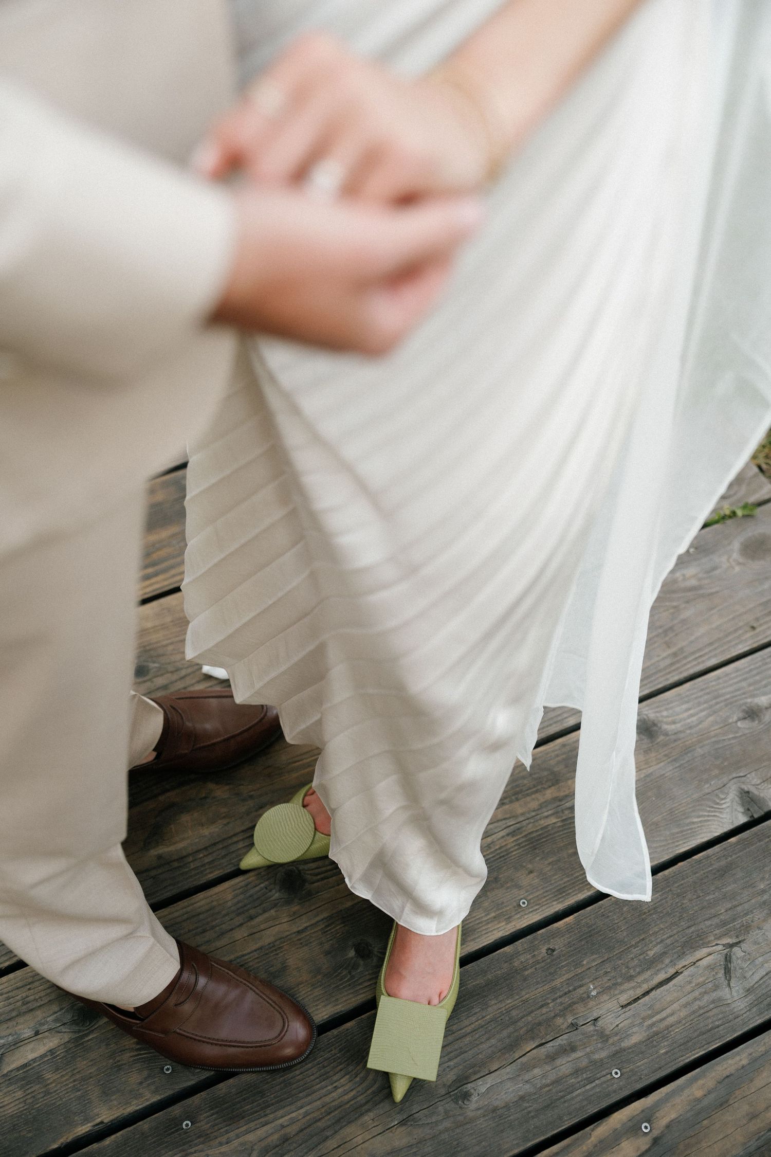 Detail shot of wedding dress hem and shoes on rustic wooden deck boards.