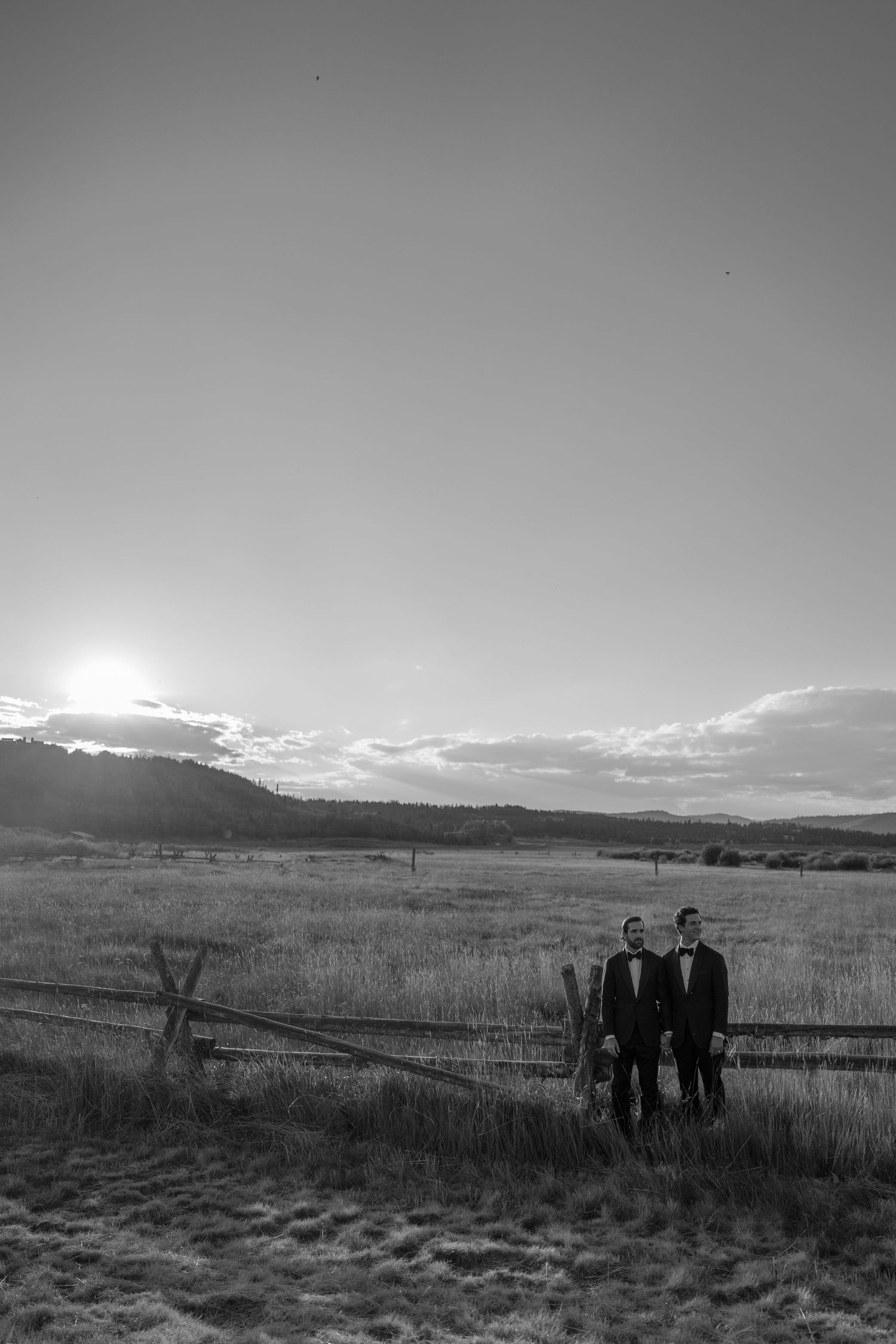 Black and white landscape photo of figures standing in an open prairie field.