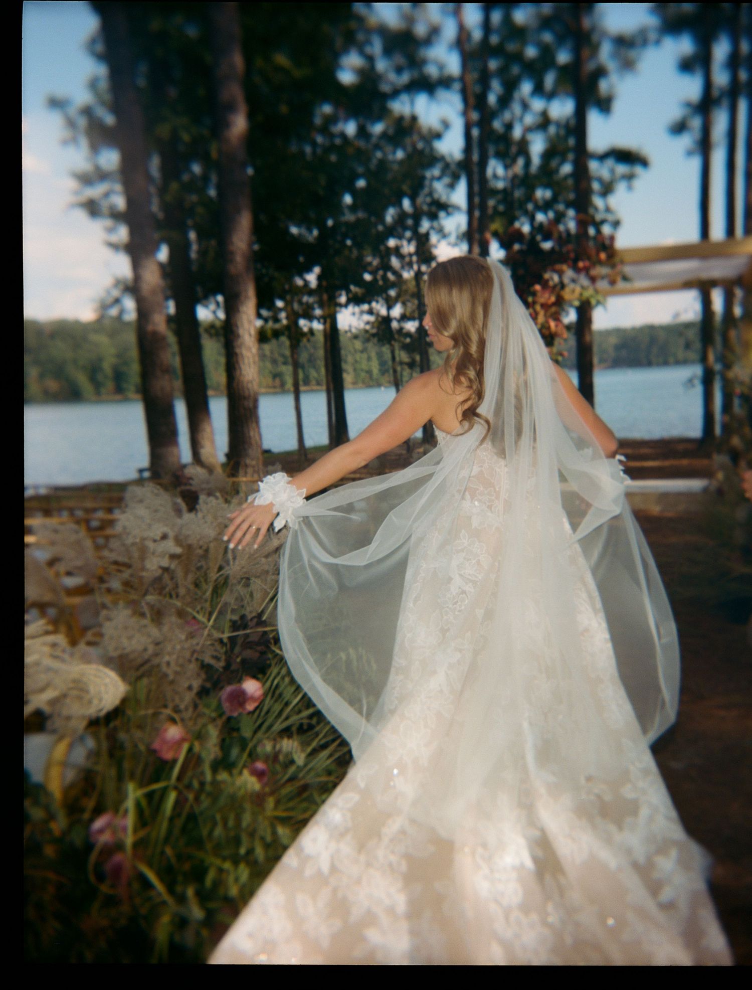 Flowing white wedding dress captured against lakeside forest backdrop.