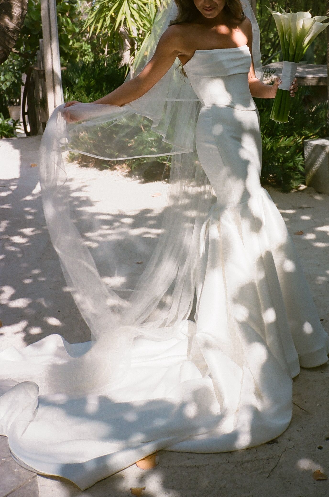 Flowing white wedding dress twirling in dappled sunlight under garden greenery.
