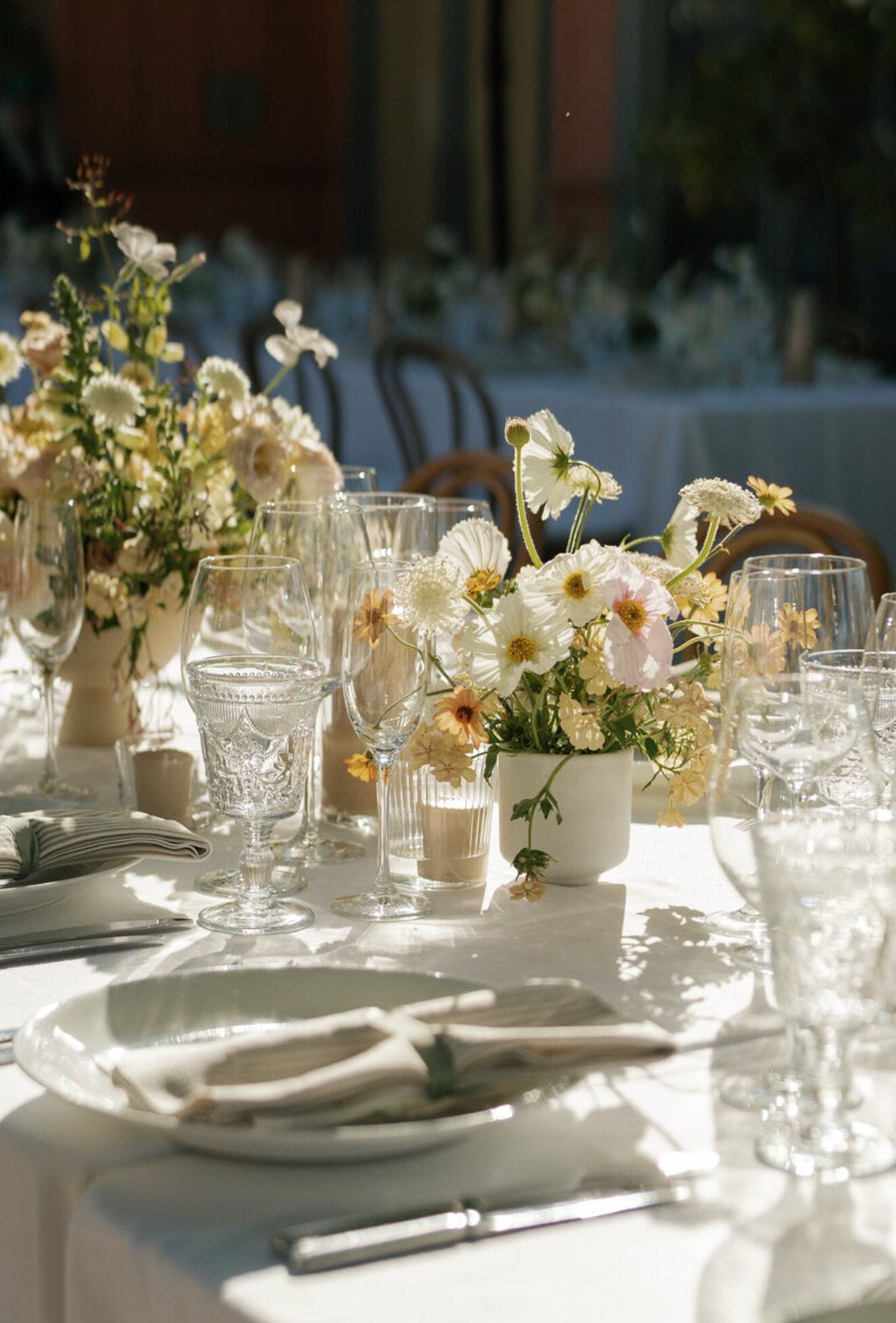 Elegant table setting with white flowers and crystal glassware in natural sunlight.
