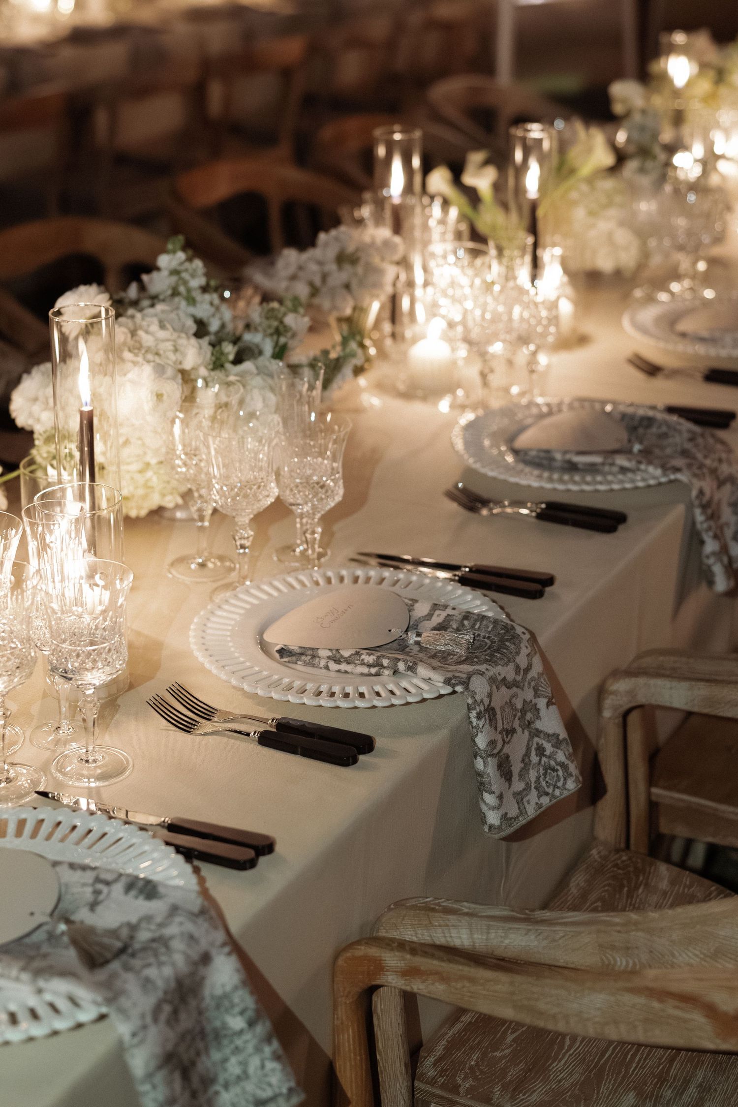 Elegant place settings with crystal glasses and white floral centerpieces at a wedding reception.