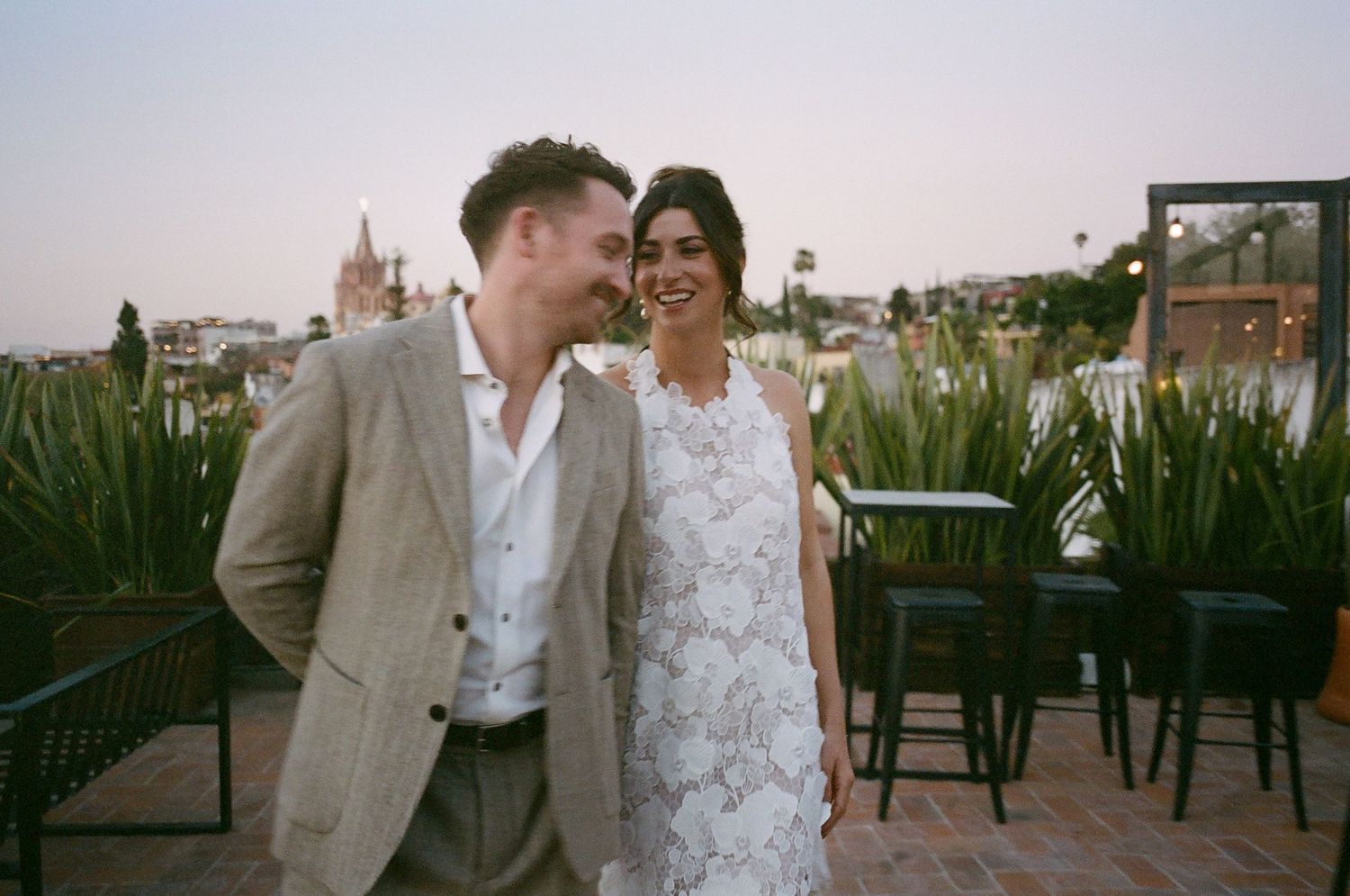 Couple in wedding attire sharing a romantic moment on a rooftop terrace at sunset.