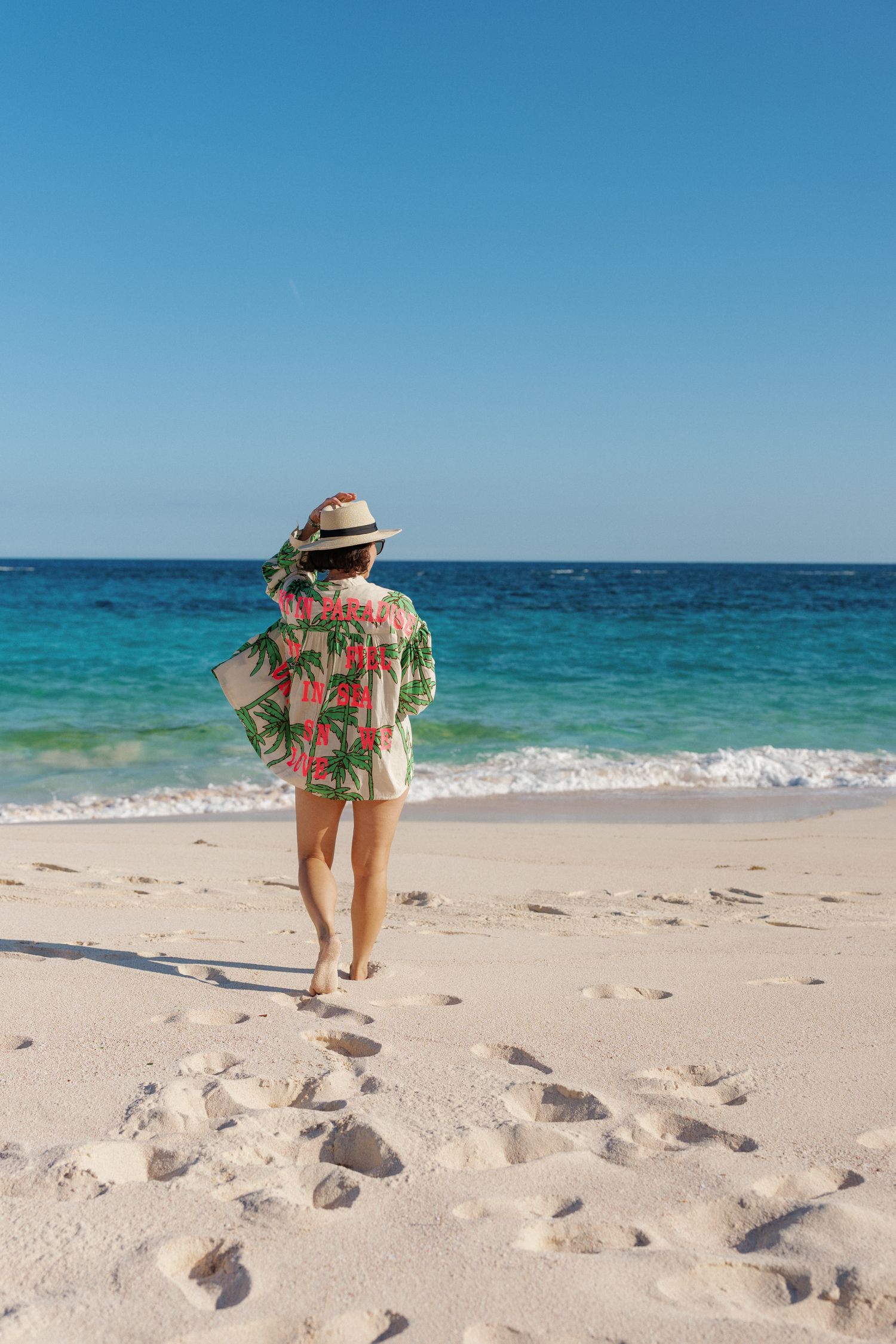 A woman in a colorful dress walking on a sandy beach.