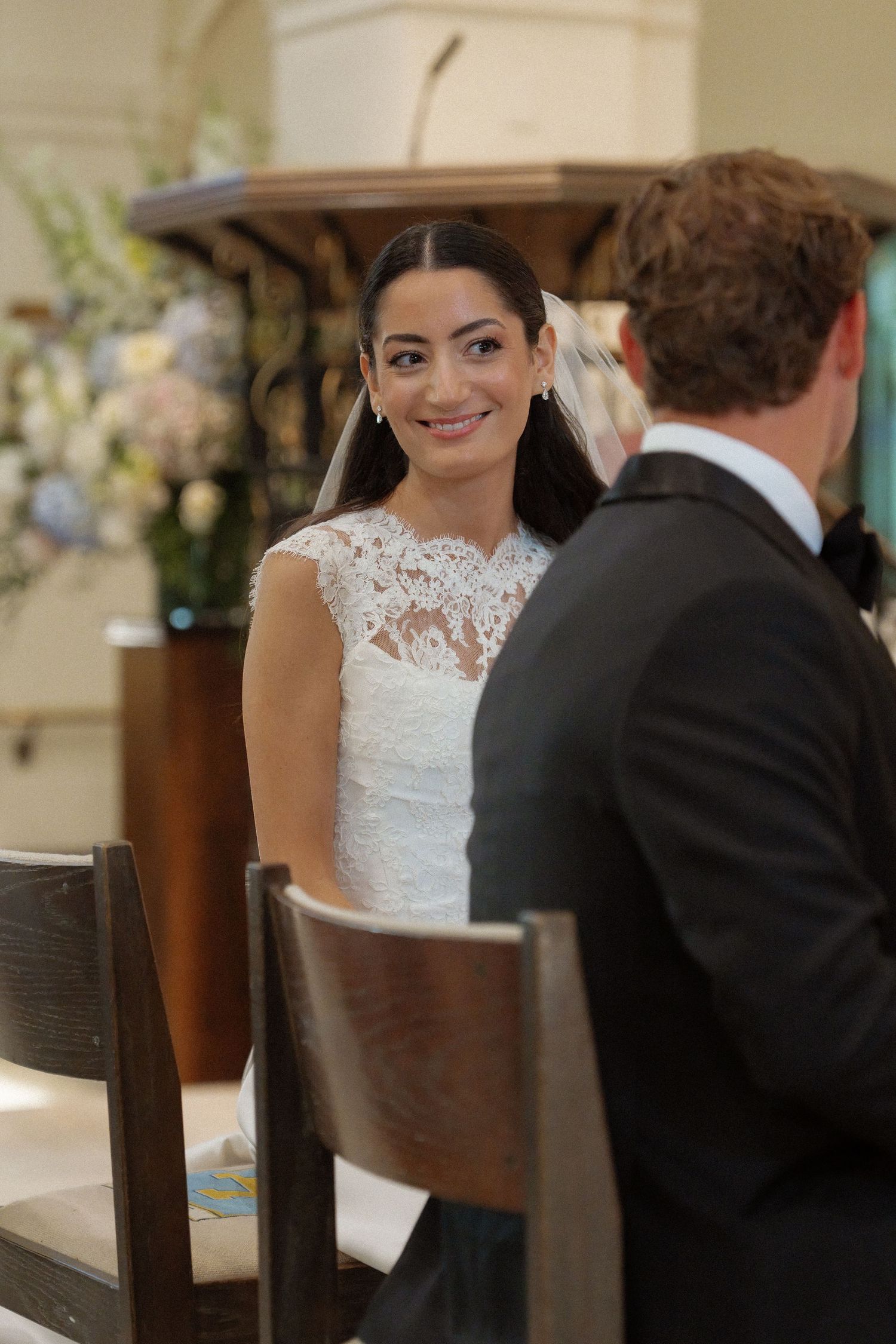 Smiling bride in lace wedding dress gazing at groom during ceremony.