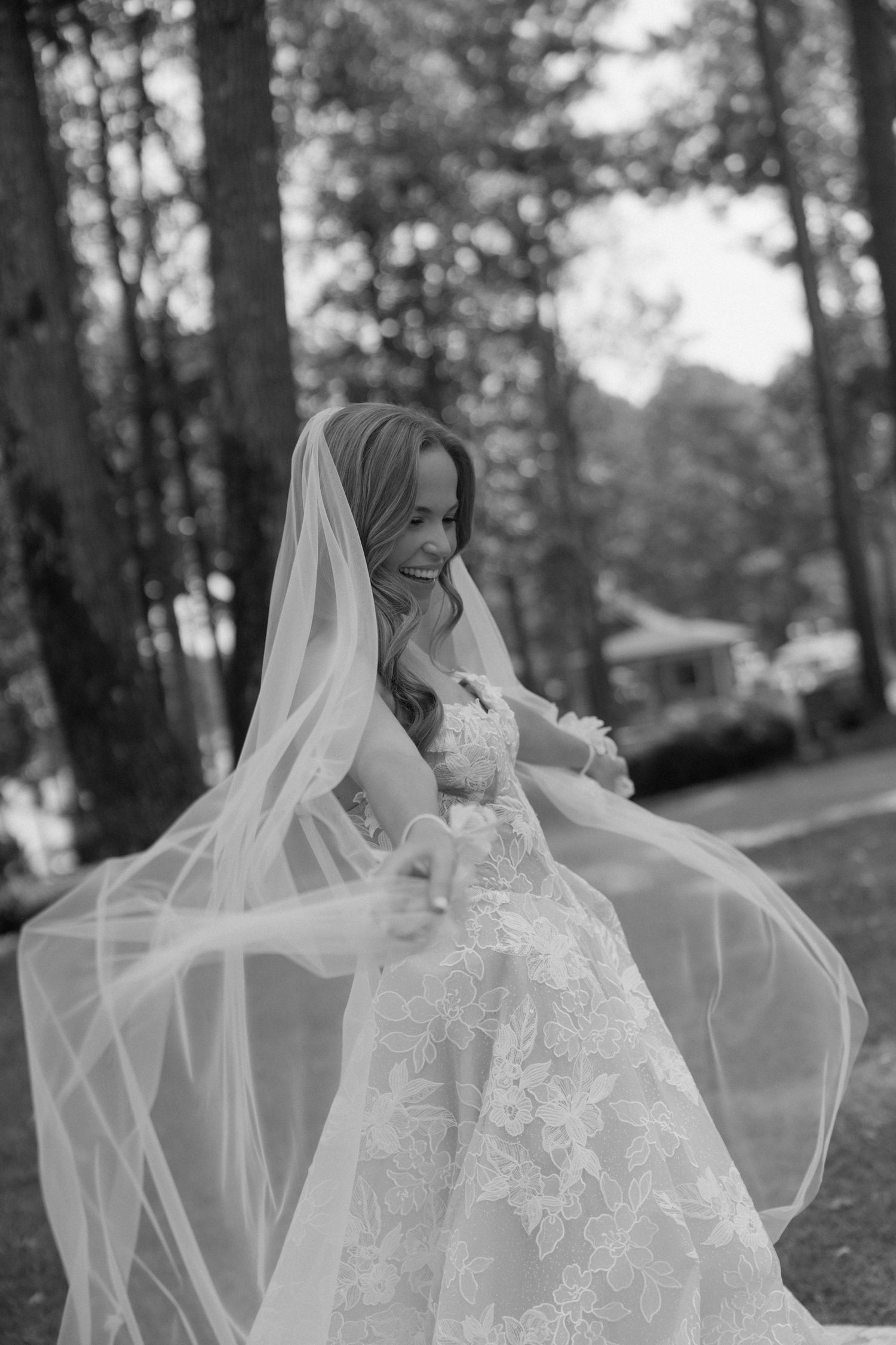 Flowing white wedding dress and veil captured in black and white among trees.